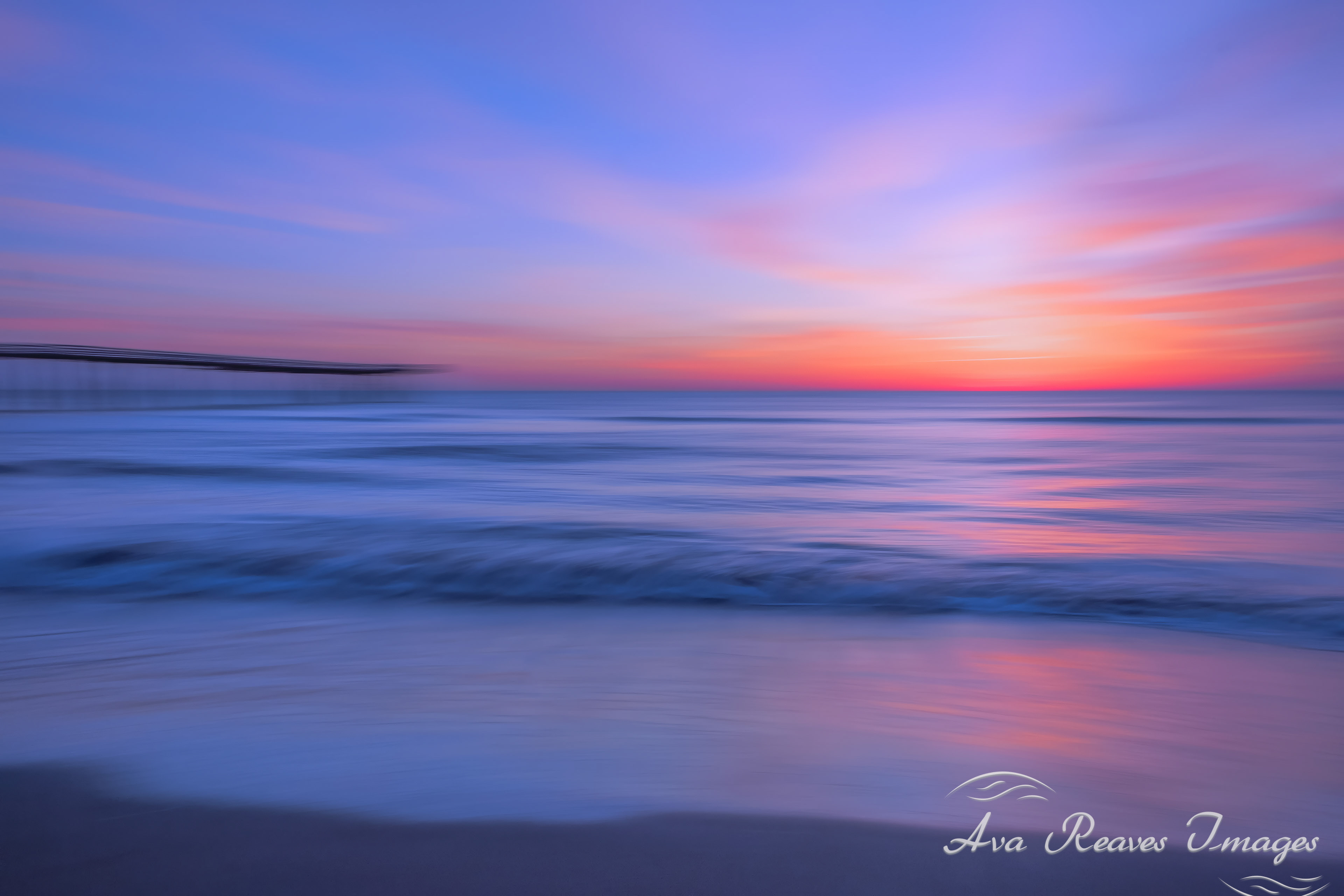 Intentional camera movement photo of a beach pier against a vibrant orange and pink sunrise sky.