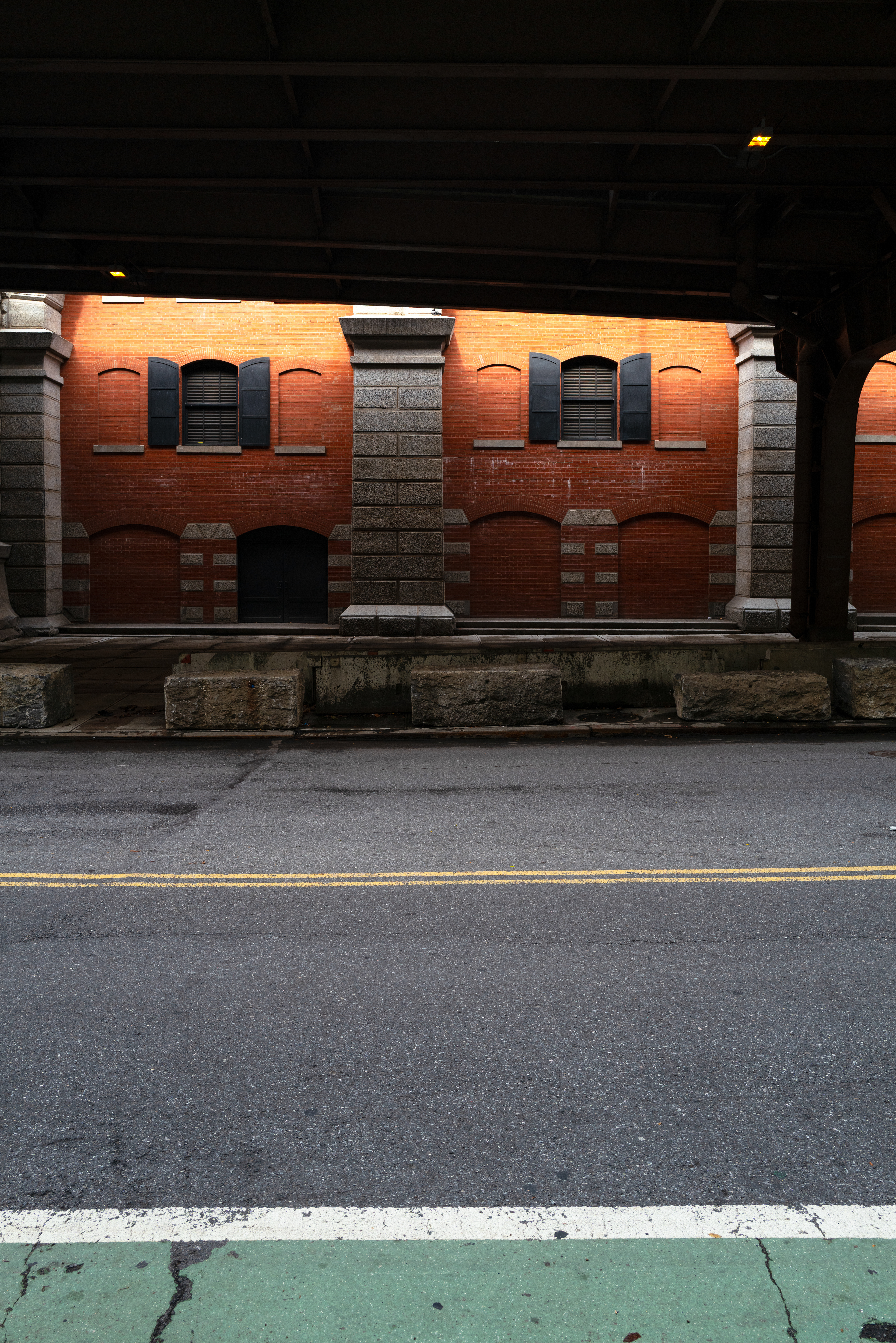 Cette photo, réalisée avec un Leica Q2, a pour but de montrer les jeux de couleurs et de lumière que l'on trouve en ville. Une partie de l'image présente une dominante orange, tandis que l'autre est teintée de vert. Une ligne jaune traverse le bitume, offrant un contraste de couleurs intéressant. This photograph, taken with a Leica Q2, aims to showcase the interplay of color and light found in an urban environment. One part of the image is dominated by warm orange tones, while the other is tinted green. A yellow line cuts across the asphalt, creating an interesting color contrast