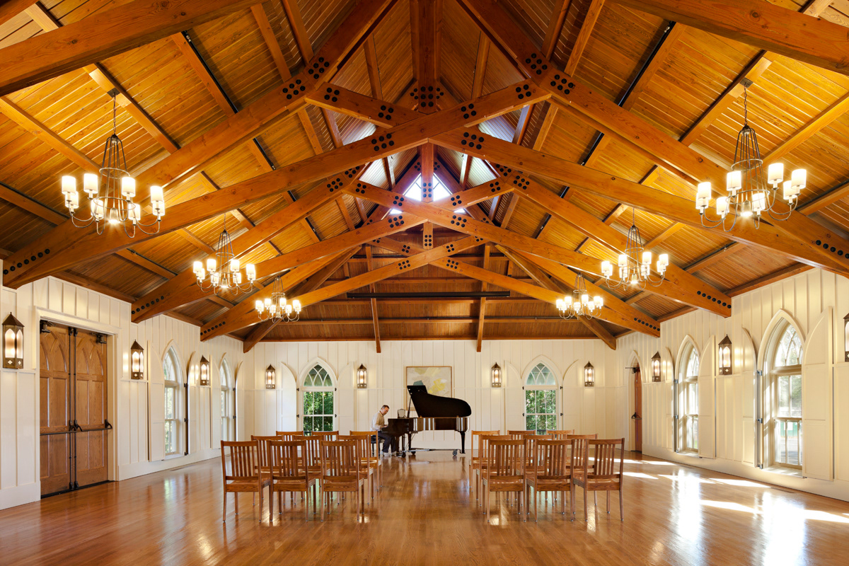 Parish Hall interior with board and batten walls, gothic arch windows and exposed stained wood trusses.
