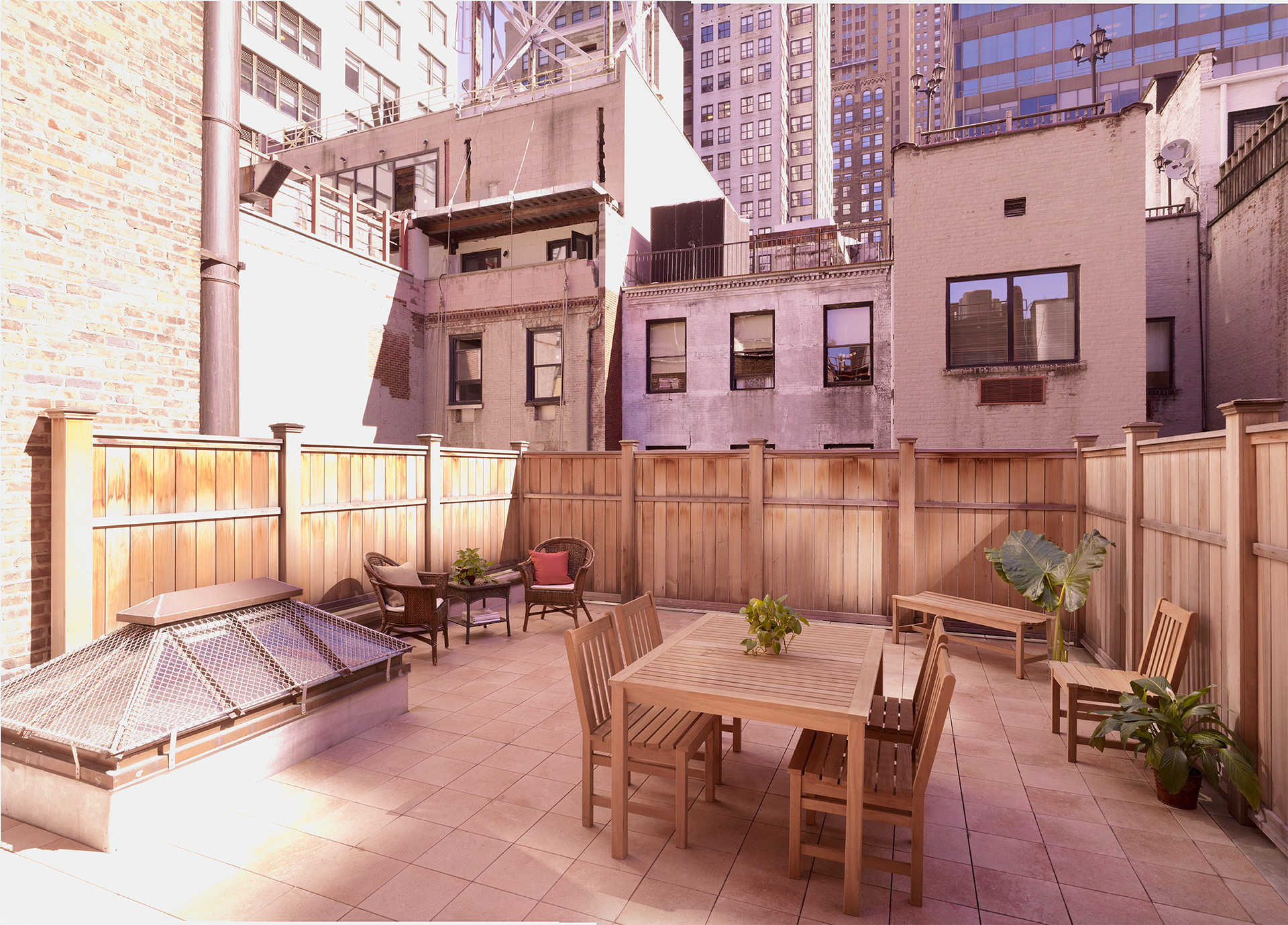 NYC townhouse roof terrace with table, skylight and a cedar fence.