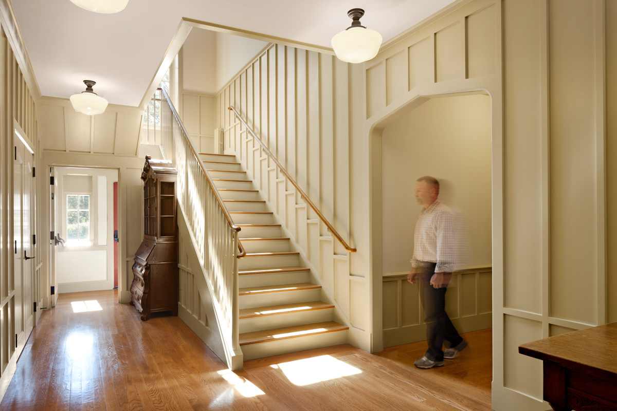 Parish Hall entry hall with board and batten paneling, shaker style stair, stained oak floors, and schoolhouse lights.
