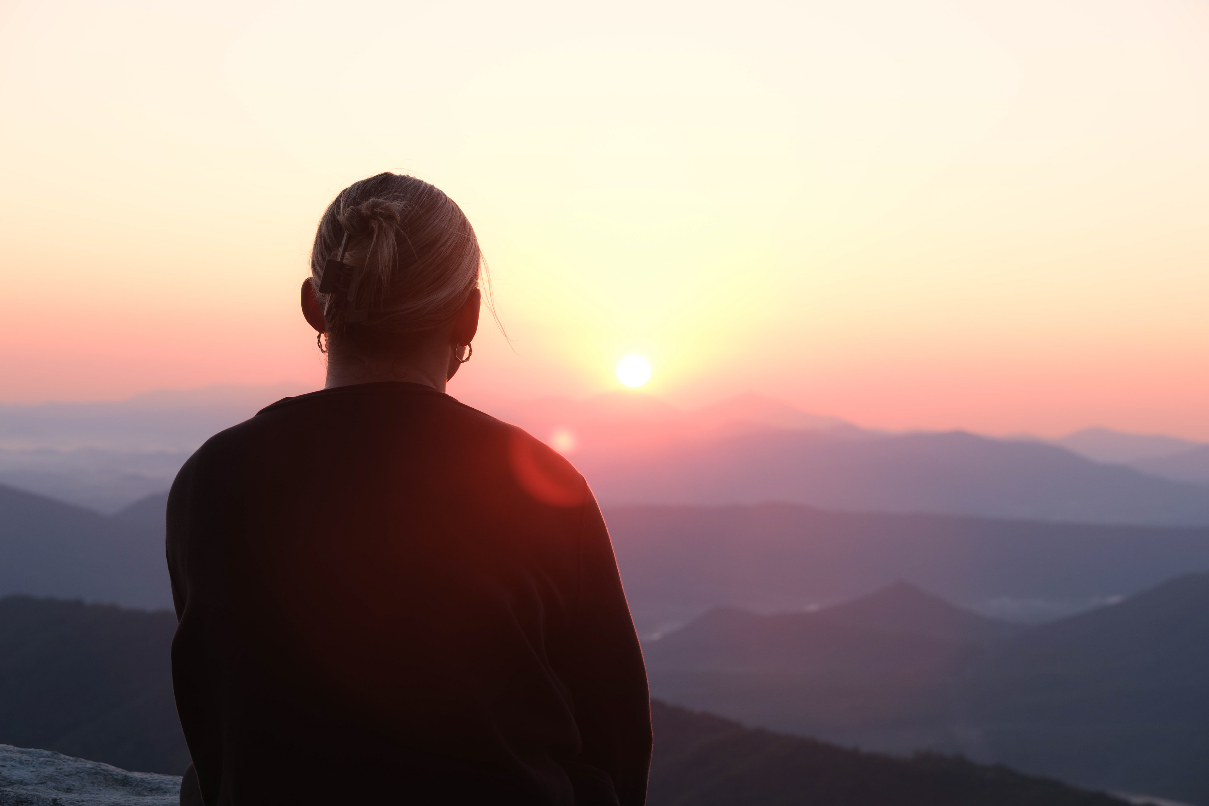 A woman observing the sunrise atop a mountain