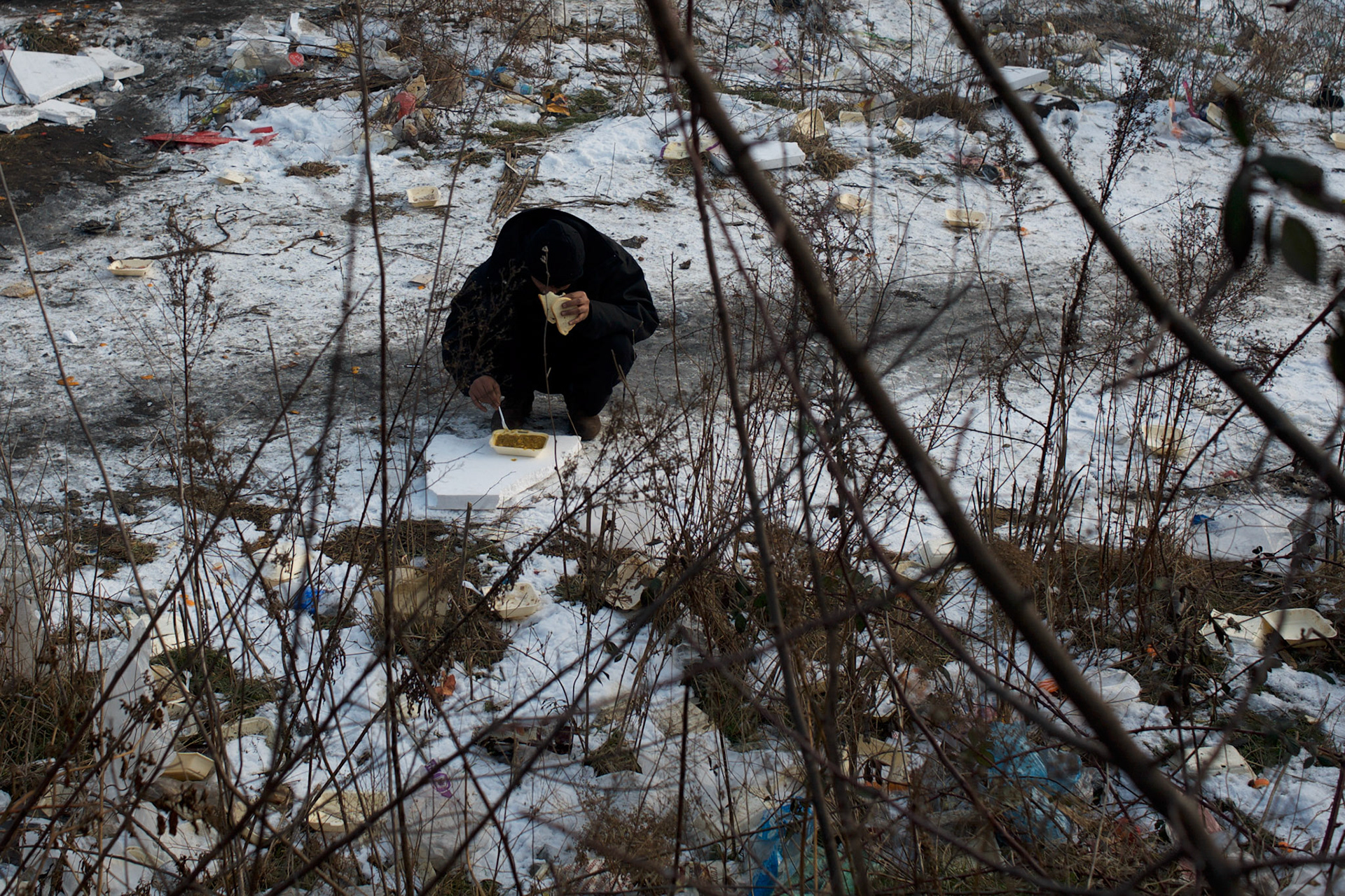 A migrant eats his meal in the frozen ground outside the old warehouses near Belgrade's main railway station. Volunteer groups provide a daily meal to the thousands of refugees living here. For the majority, this is the only daily meal they have access to.