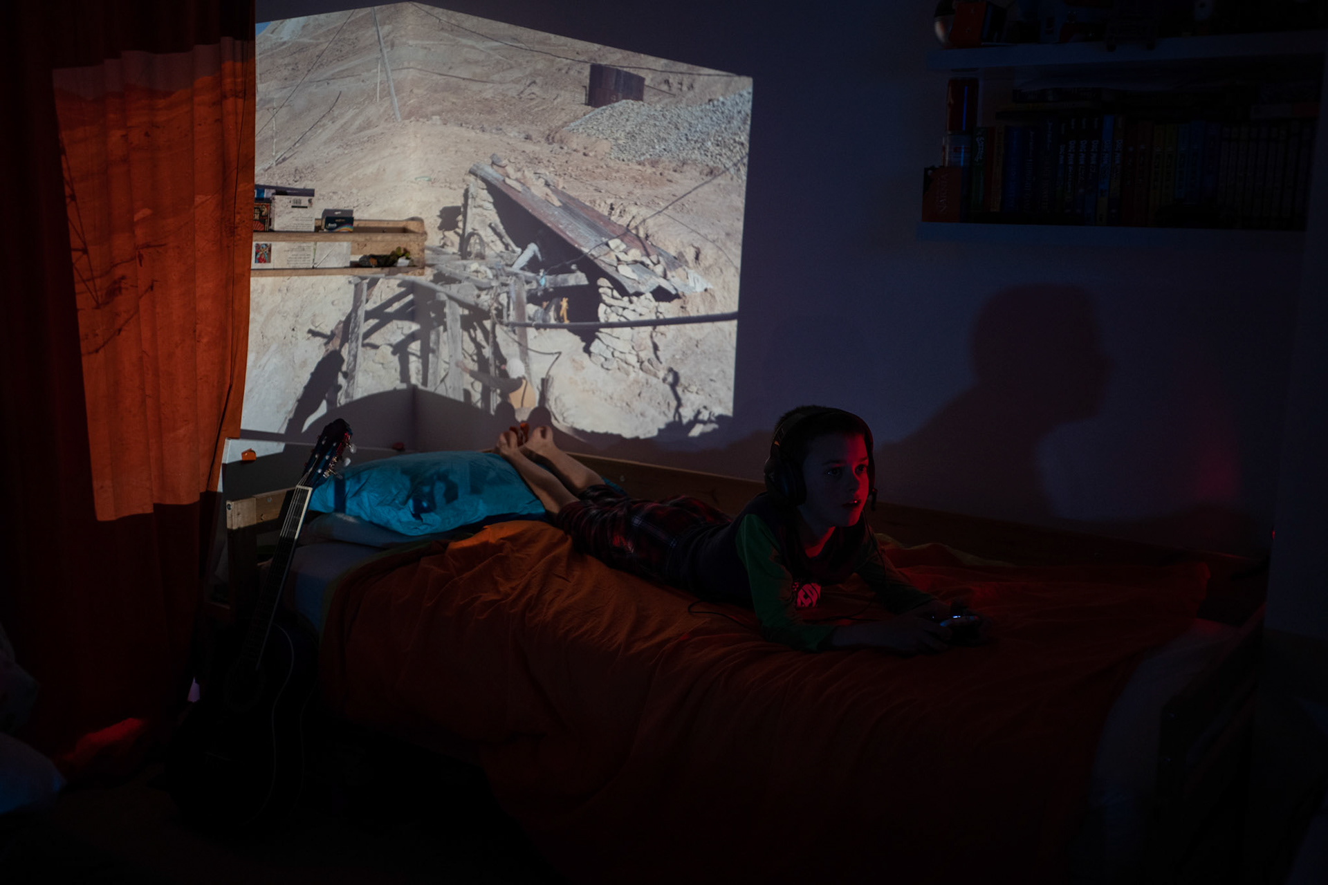 Oliver playing Xbox with a slide of the silver mines in Potosi projected onto his bedroom walls.