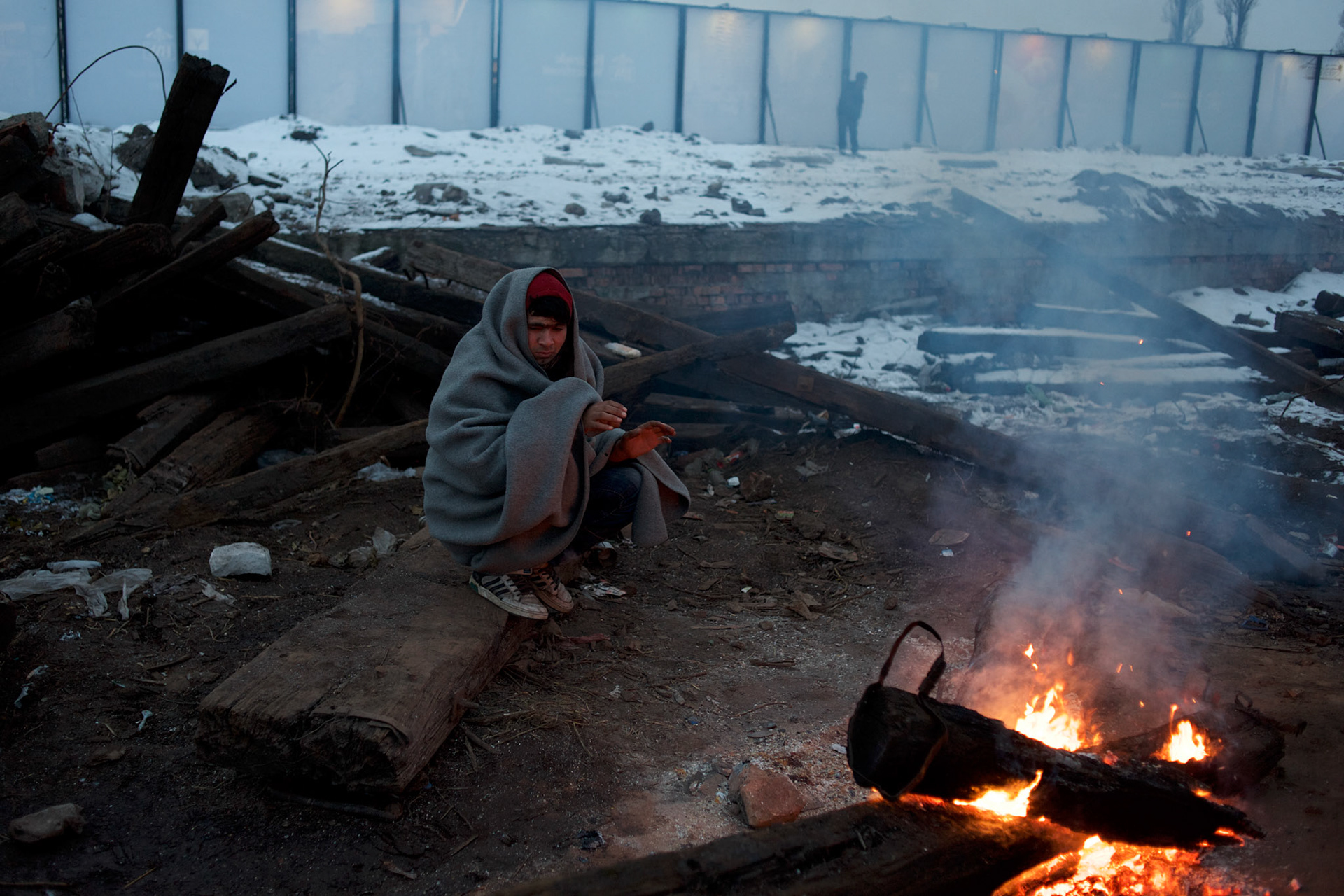 A migrant keeps warm near a open fire outside the abandoned warehouses in central Belgrade. The toxic old railway sleepers scattered around the area are been burned in bonfires used as main source of heat inside and outside the makeshift shelters.