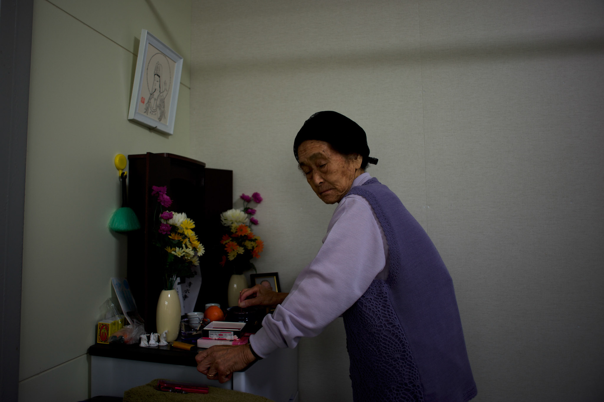 Grandmother Abe, a Togura resident who become a widower when her husband died during the 2011s tsunami that struck over the coastal areas of Japan, prays at the shrine in memory of her husband in the family's pre-fabricated house.