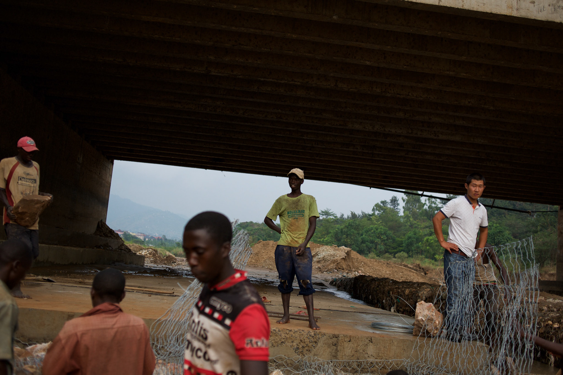 Local men are monitored by a Chinese engineer during the construction of a dam to prevent the erosion of the support pillars of a bridge in  central Bujumbura, Burundi.