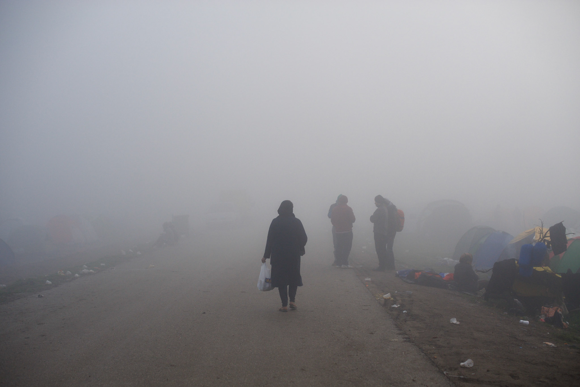 Migrants walk by the border post between Greece and Macedonia during a foggy morning in Idomeni, Greece.