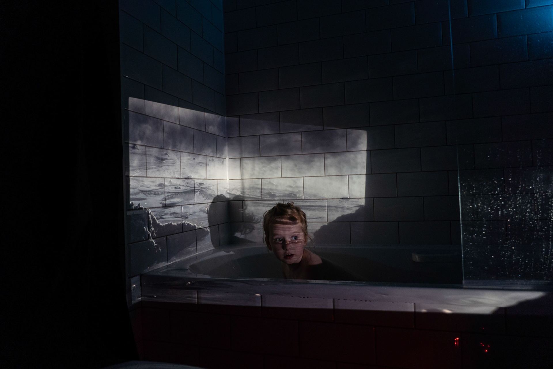 Millie taking a bath with an image of bubbling boiling mud of a geyser in the Bolivian Altiplano projected onto the bathroom tiles.