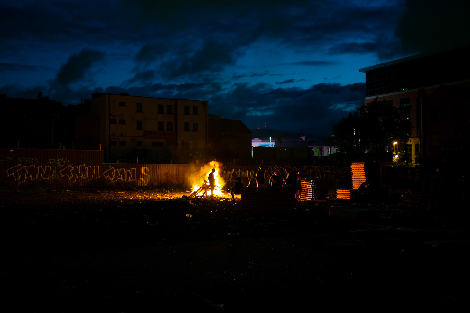 Young men from Donegall Pass, a predominantly working-class loyalist community in inner-city Belfast, keep watch through the night over the local bonfire being built for the Twelfth of July celebrations in Belfast, Northern Ireland, on July 9, 2021.