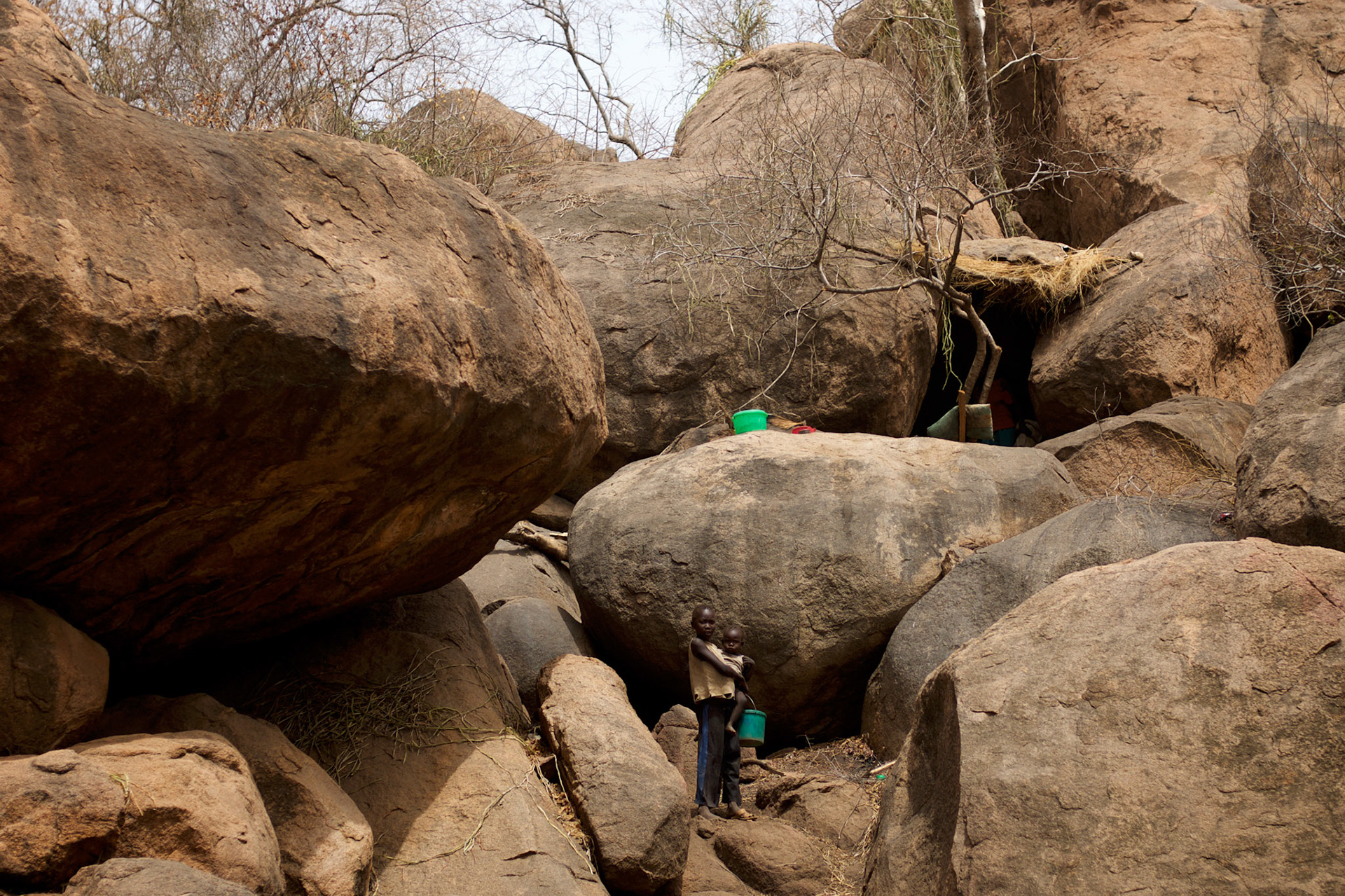 Children stand outside a cave used as shelter against bombardments by Sudan's Army Forces airplanes near the Nuba village of Tess in South Kordofan.