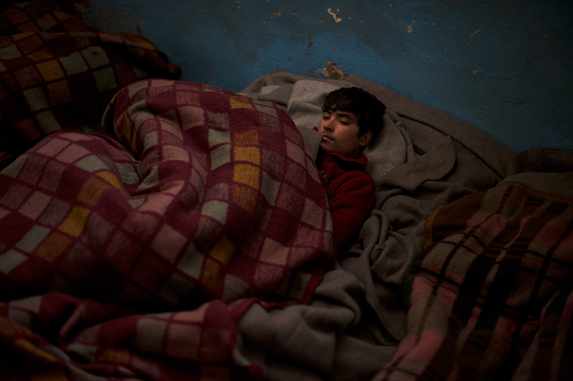 A young migrant sleeps wrapped in blankets in one of the abandoned warehouses in central Belgrade. Due to the extreme low temperatures typical of a Serbian winter, many migrants spend the days by the fire or wrapped under blankets.