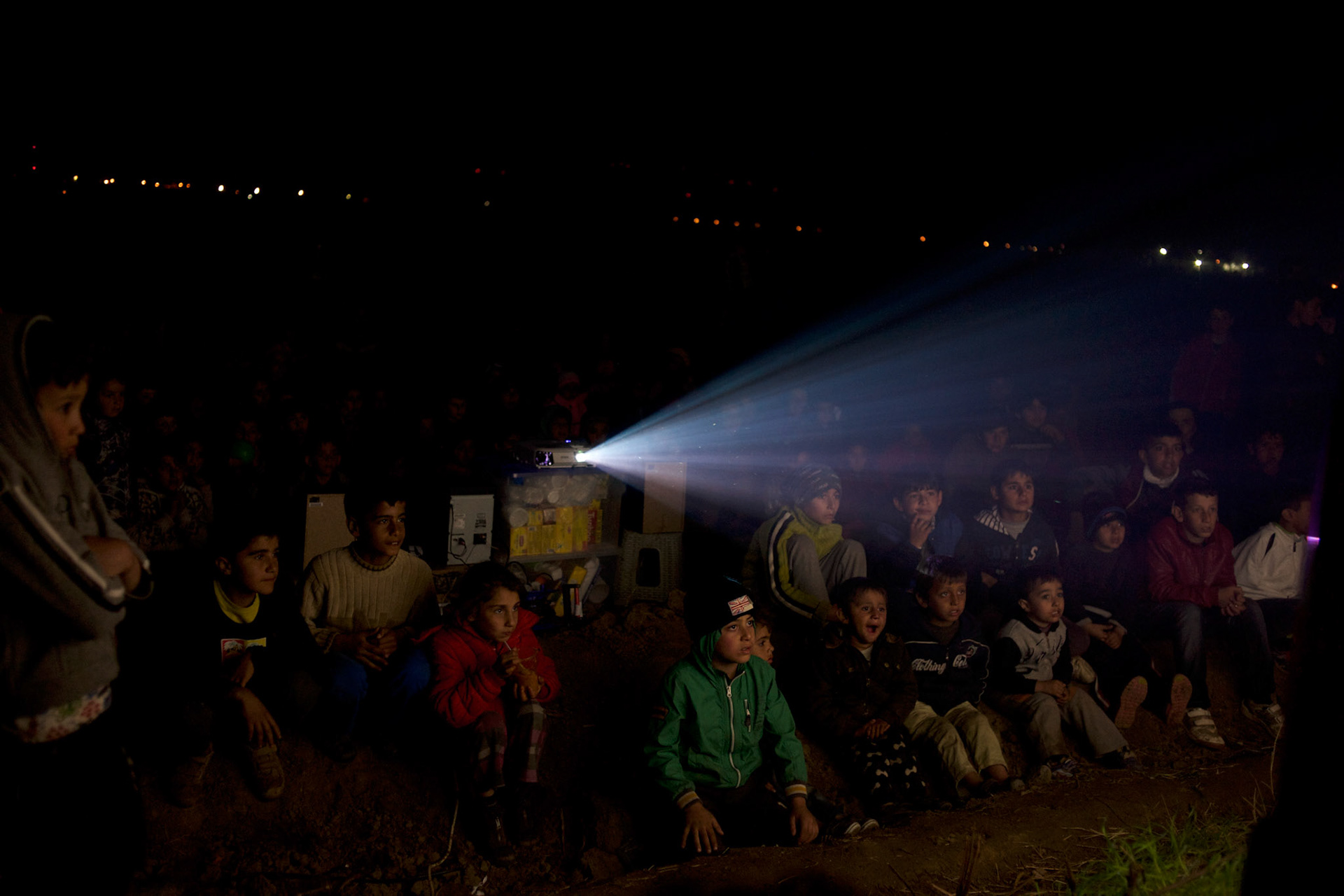Refugee children assist to an open air cinema session set up by volunteers at the Greek-Macedonian border in Idomeni, Greece. Around 13,000 migrants and refugees, mostly from the Middle East and African nations, are believe to be stranded here awaiting a chance to proceed their journey towards Germany and other northern European countries.