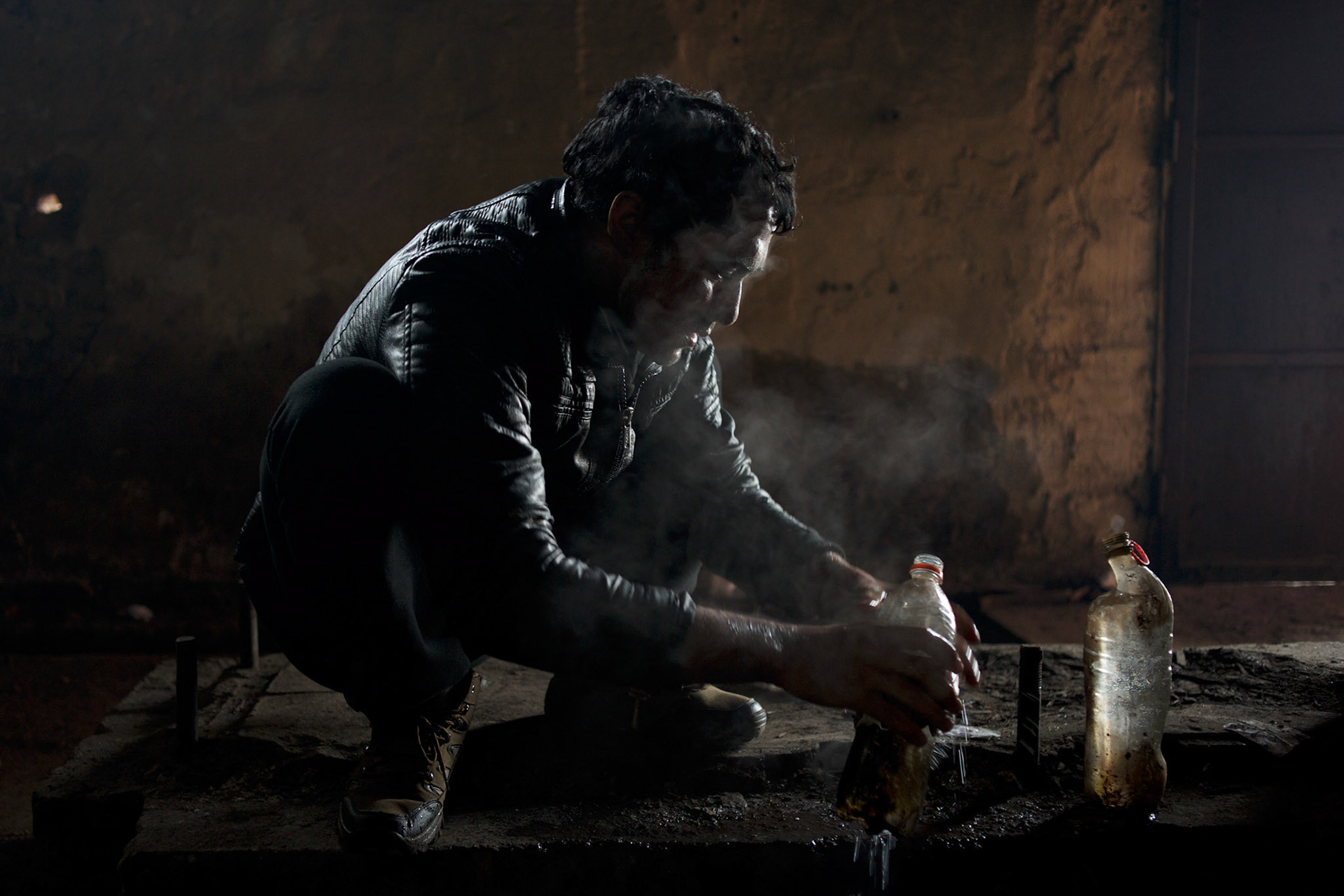 An afghan man washes himself using water heated in plastic bottles thrown to open fire. The hundreds of migrants living in the makeshift shelters are deprived of basic sanitary facilities.