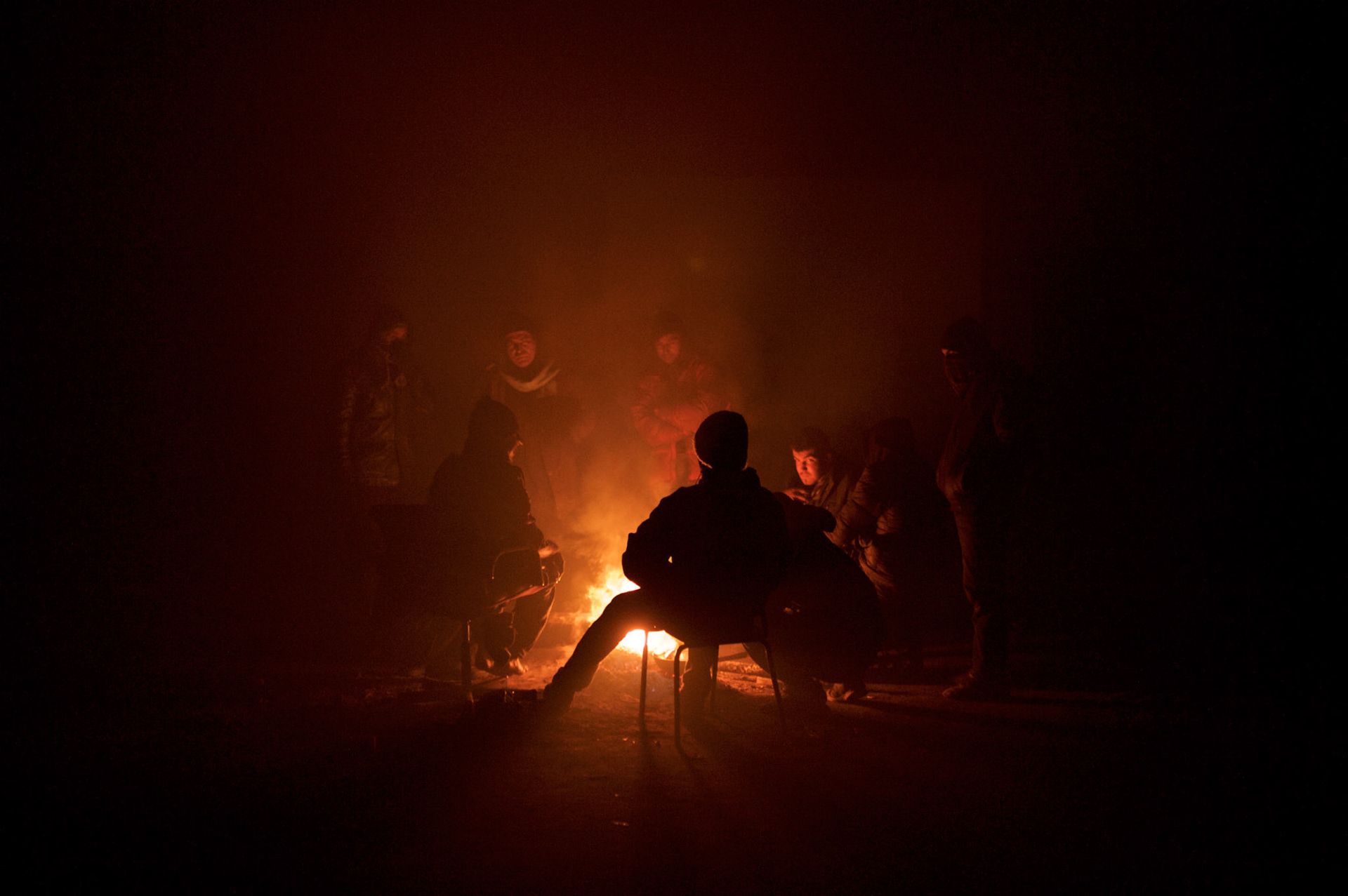 A group of migrants socialise covered with smoke around a open fire inside a makeshift shelter near Belgrade's main railway and bus stations.