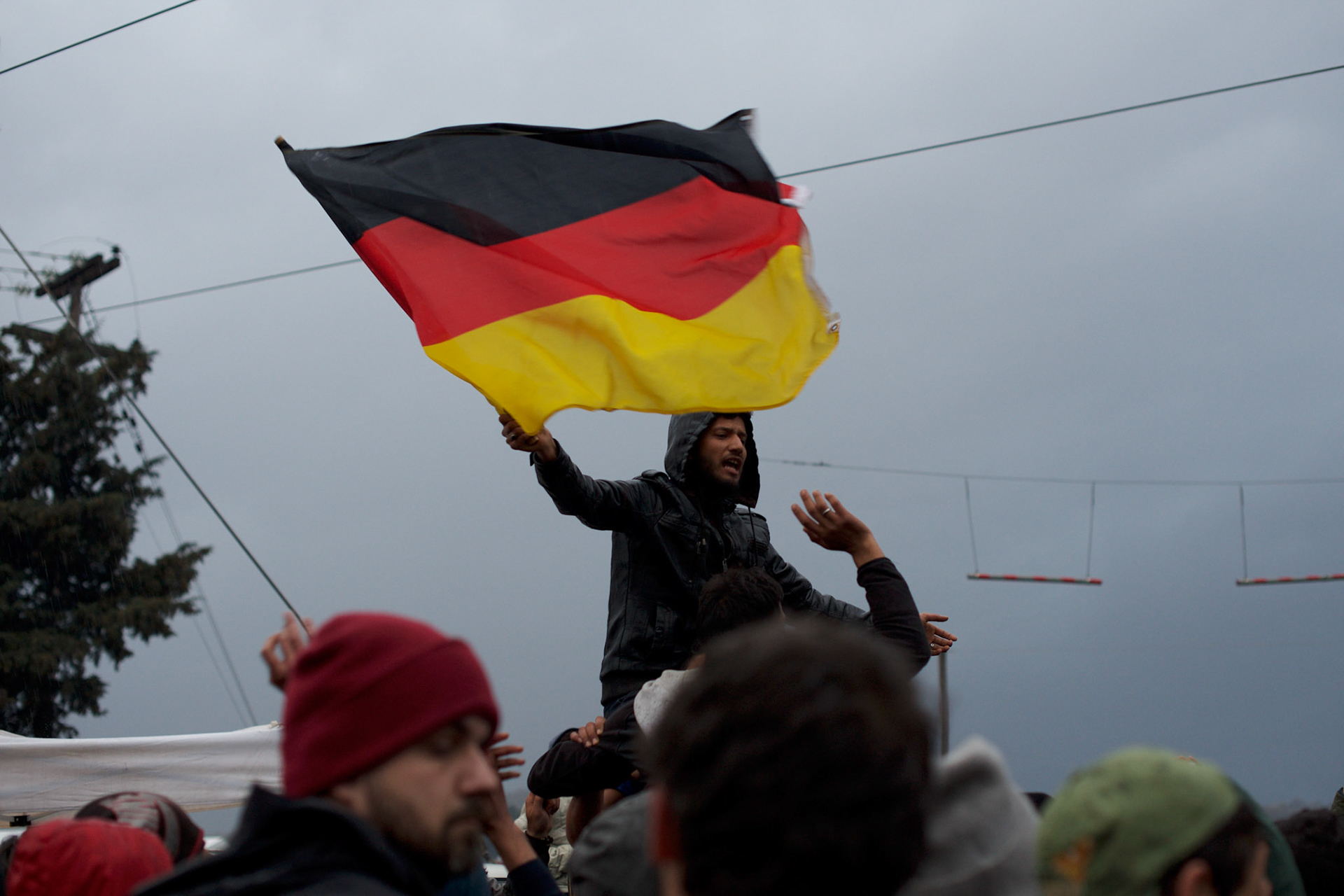 A refugee is seen waiving a German flag during a demonstration at the Greek-Macedonian border near the Greek village of Idomeni. Around 13,000 migrants and refugees, mostly from the Middle East and African nations, are believe to be stranded here awaiting a chance to proceed their journey towards Germany and other northern European countries.