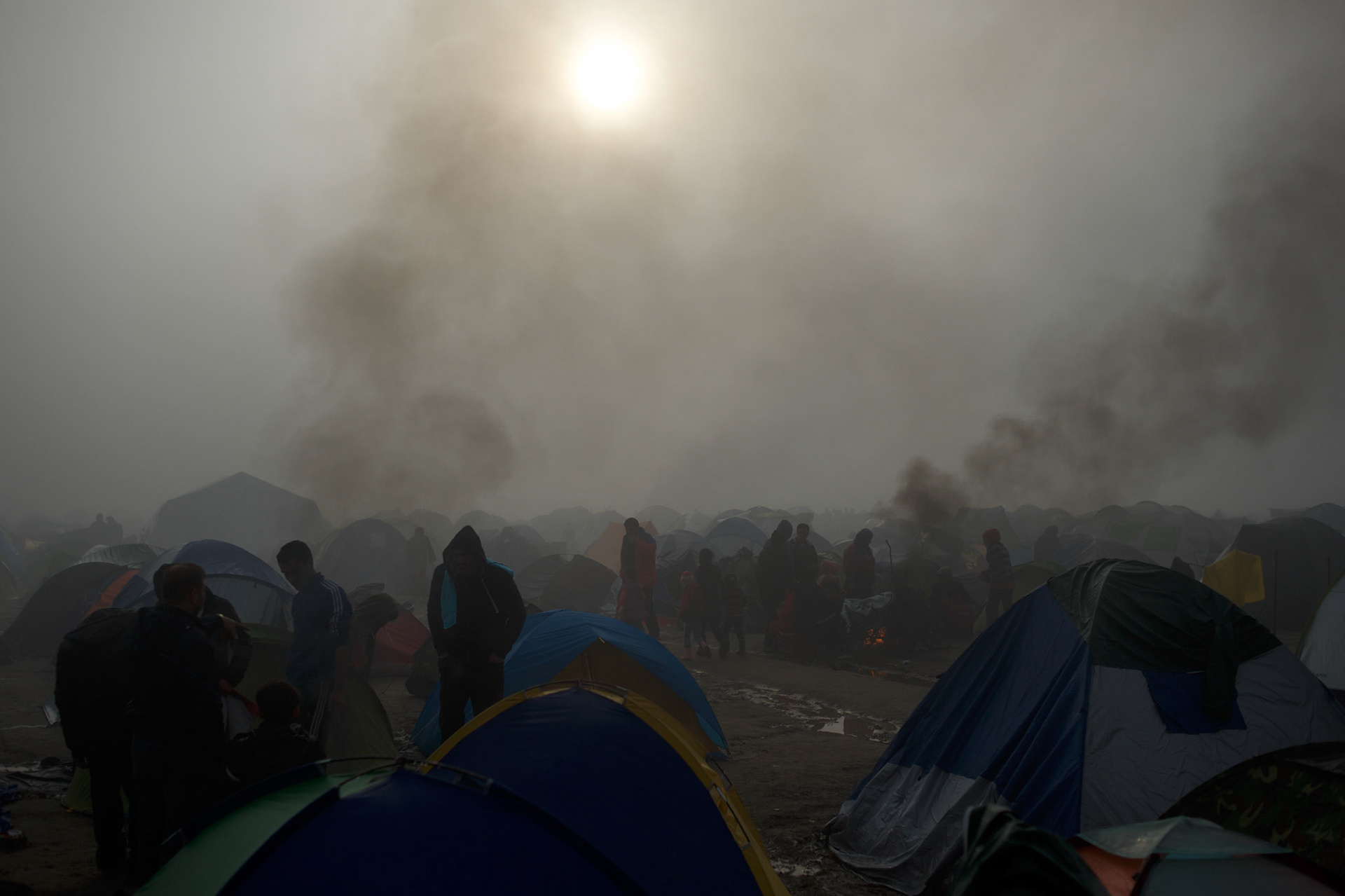 Syrian refugees are seen standing outside their tents, after a night of heavy rain fall, at the Greek-Macedonian border station of Idomeni, Greece. Around 13,000 migrants and refugees, mostly from the Middle East and African nations, are believe to be stranded here awaiting a chance to proceed their journey towards Germany and other northern European countries.