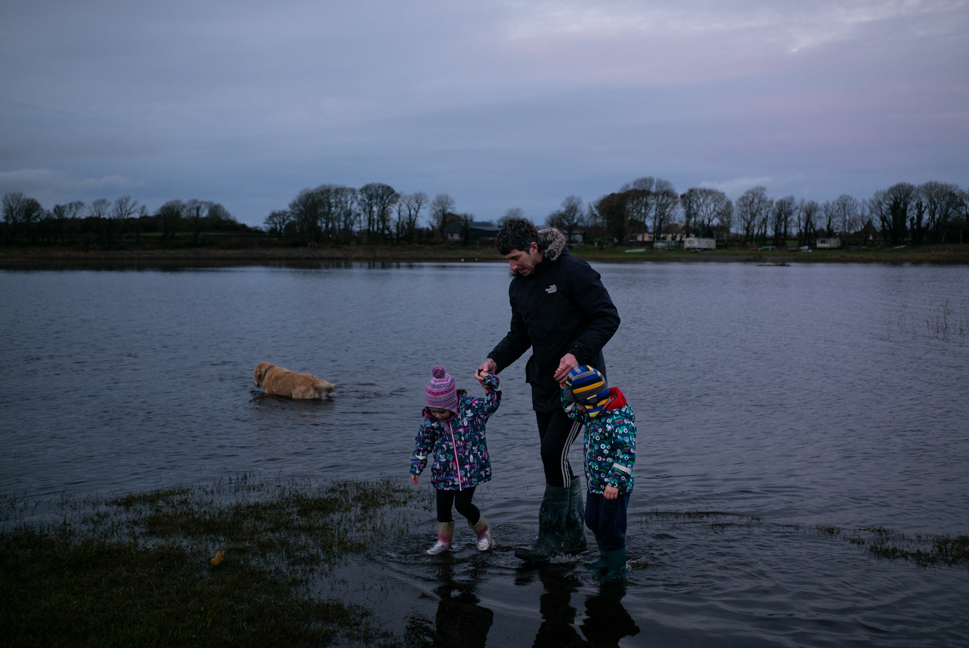 BALLINA, IRELAND - NOVEMBER 28, 2021: Faith Healer, Andrew Keane and his children Élia and Kay, walk by the lake leading to their house in Cloghans, a small location outside Ballina in County Mayo, Ireland. A construction worker by trade, Mr. Keane is just one of hundreds dotted across the country who are healers or have “the cure” as it’s commonly known here. Some, like him, are seventh sons, believed for generations to be healers, but others are keepers of customs passed down through their families that range from rituals, prayers and charms to herbal tinctures that are offered up as remedies for everything from burns to sprains to shingles and other ailments. CREDIT: Paulo Nunes dos Santos for The New York Times