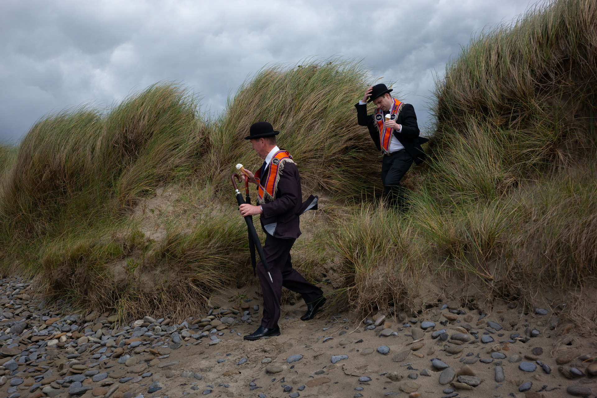 Two Orangemen eating ice cream emerge from the dunes after the annual Orange Order parade at Rossnowlagh Beach in Co. Donegal, Ireland, on July 6, 2024. Around 50 Orange lodges from Ireland and Northern Ireland paraded down a country lane toward the seaside village of Rossnowlagh on Saturday, the only annual Orange Order parade in the Republic of Ireland. Thousands attended the parade, which traditionally takes place on the Saturday before the main Twelfth demonstrations in Northern Ireland.