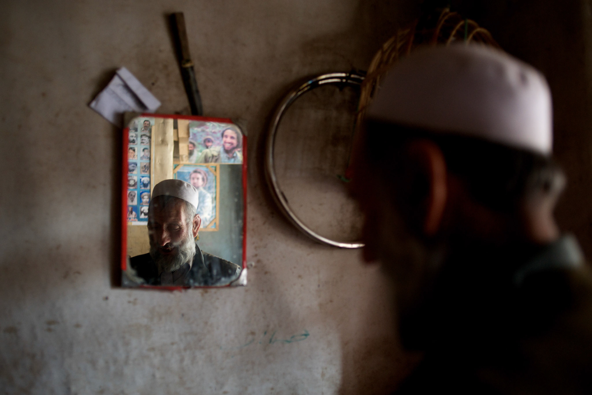 November 06, 2012 - Kabul, Afghanistan: Reflexion of a local merchant on a mirror in a shop at the bird's bazaar. In the back wall, posters of the late mujahideen commander, Ahmad Shah Massoud. (Paulo Nunes dos Santos)