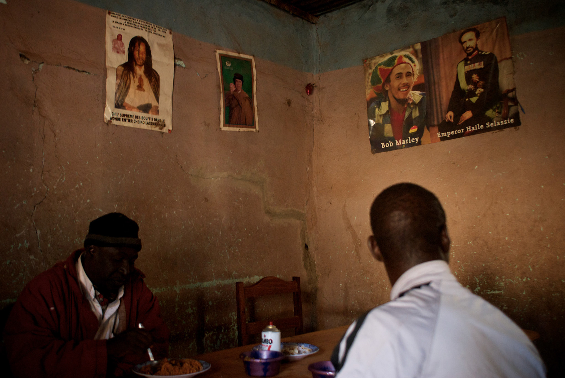 January 19, 2013 - Niono, Mali: Locals take lunch at a restaurant, with Kaddafi, Bob Marley and Emperor Haile Selassiei poster displayed on the wall, in Niono village, the last government controlled location before Diabaly, a city under islamist militants control since the 14th of January. In the backSeveral insurgent groups have been fighting a campaign against the Malian government for independence or greater autonomy for northern Mali, an area known as Azawad. The National Movement for the Liberation of Azawad (MNLA), an organisation fighting to make Azawad an independent homeland for the Tuareg people, had taken control of the region by April 2012.The Malian government pledge to the French army to help the national troops to stop the rebellion advance towards the capital Bamako. The french troops started aerial attacks on rebel positions in the centre of the country and deployed several hundred special forces men to counter attack the advance on the ground. (Paulo Nunes dos Santos)