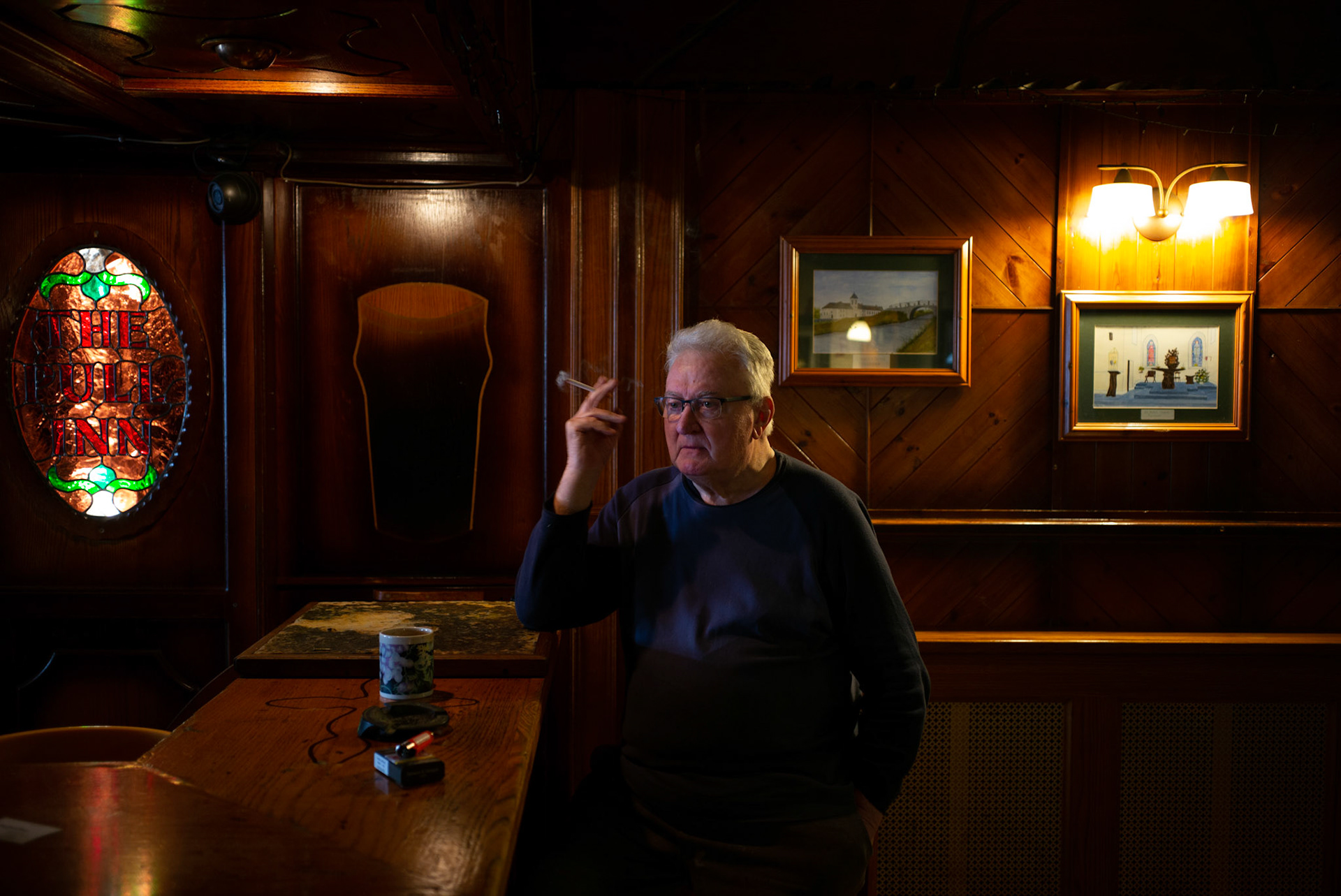 PULLOUGH, IRELAND - NOVEMBER 10, 2021: Faith Healer Joe Gallagher, smokes a cigaret in the pub adjacent to his house in Pullough, a small village in County Offaly, Ireland, where every Sunday he receives people looking for treatment for various ailments. As a seventh son, Joe, also a former monk, is known for having faith healing powers since young age. Faith healers have been around since antiquity and many Irish believe that certain people have God-given gifts to cure diseases. According to old Irish folklore, the seventh son of a seventh son has special healing powers, however, others get ‘the cure’ passed on to them by a parent or an older relative. CREDIT: Paulo Nunes dos Santos for The New York Times