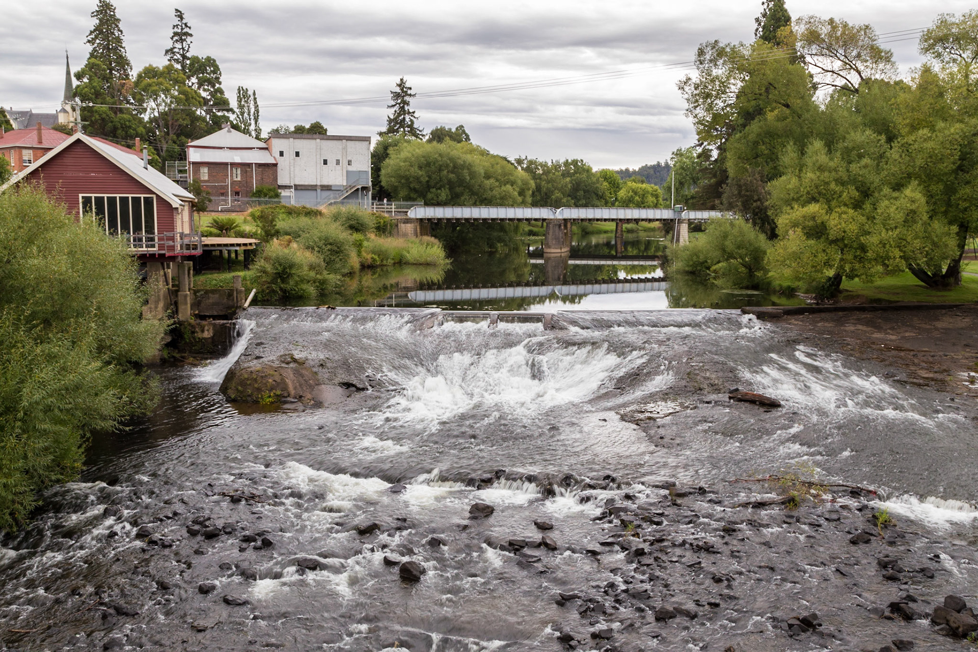 Deloraine, Meander River Weir. The weir was built around 1907 to hold back water for turning the wheel which drove the generator for Deloraine's first power station, which was in the building at the left of the picture.
