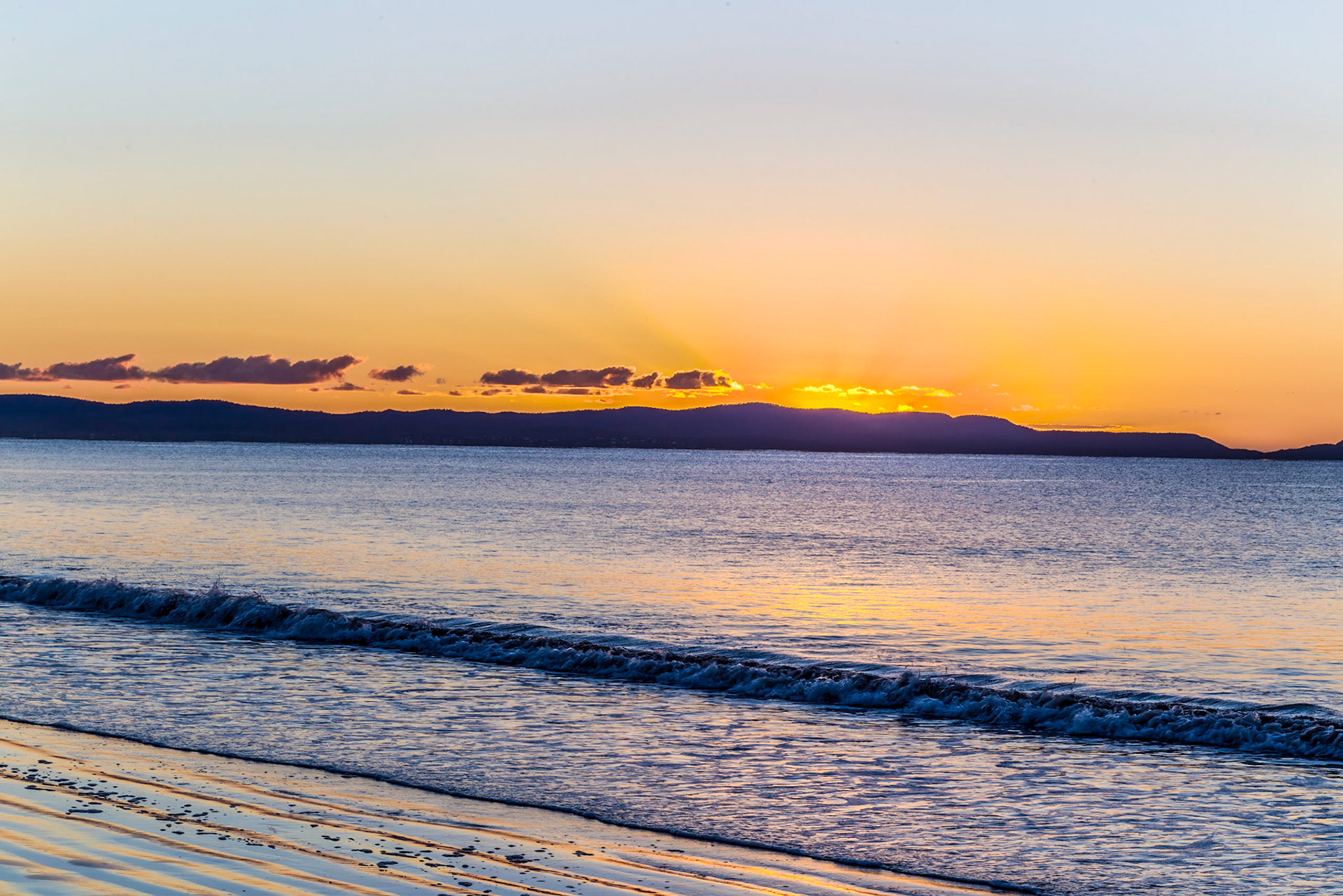 Small clouds on the eastern horizon glow brilliant gold just before the sun lifts above the horizon. Schouten Beach.