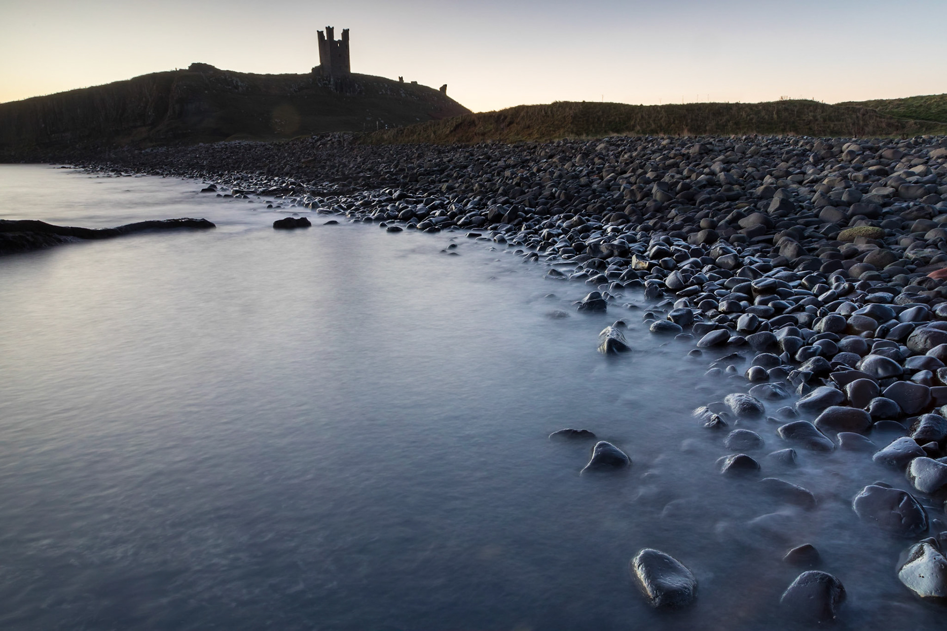 Dunstanburgh Castle in silhouette at sunrise