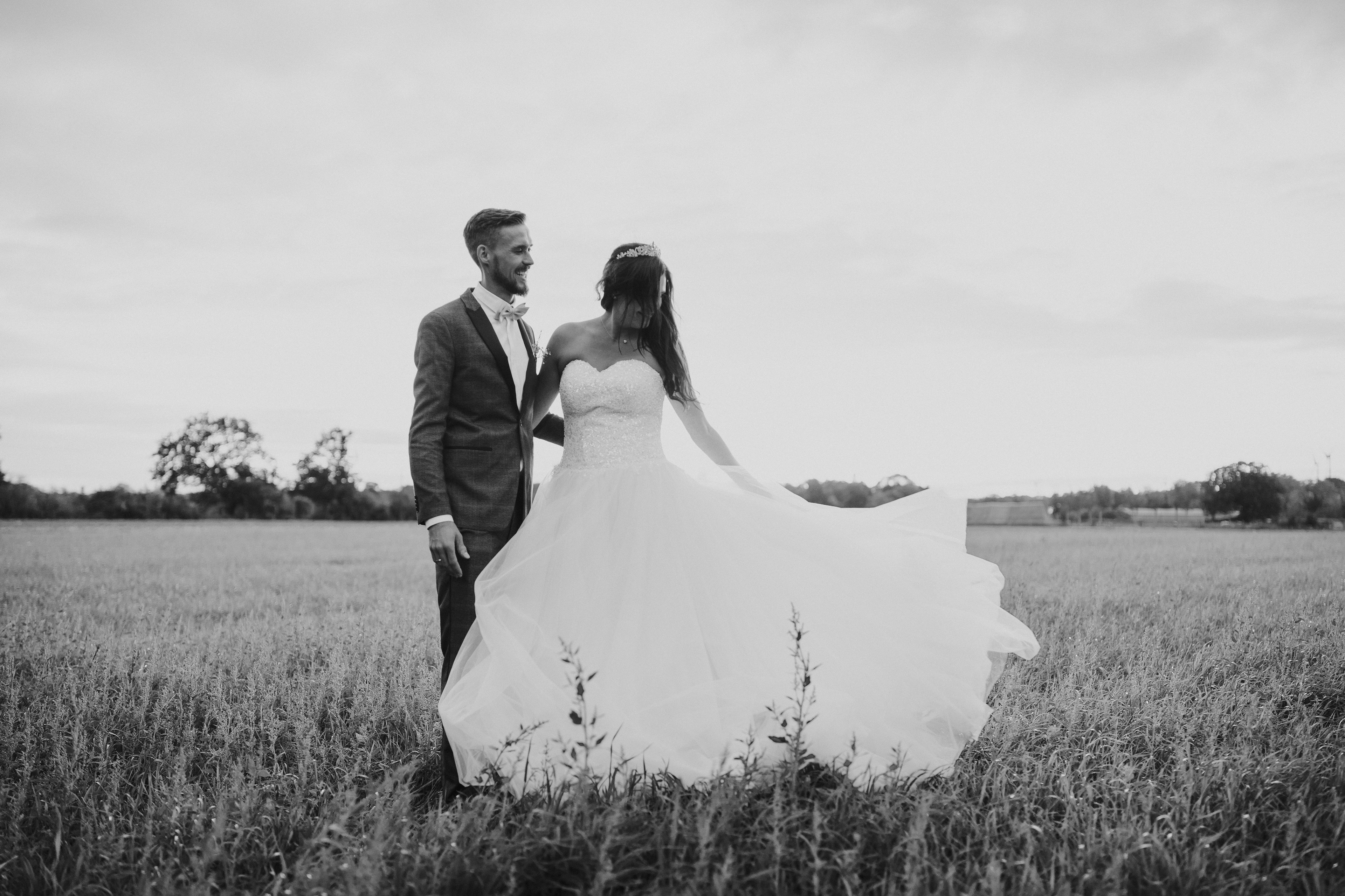 Brautpaarshooting auf einem Feld. Kleid weht im Wind.