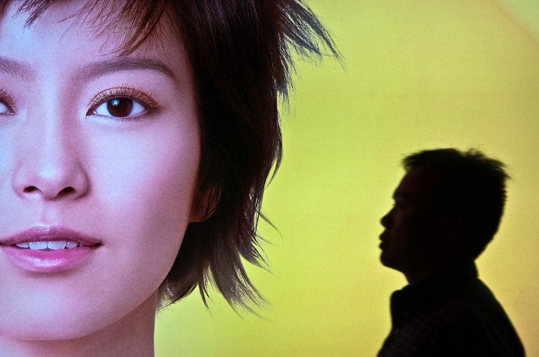 A man walking in front of a advertisement in Hong Kong. 