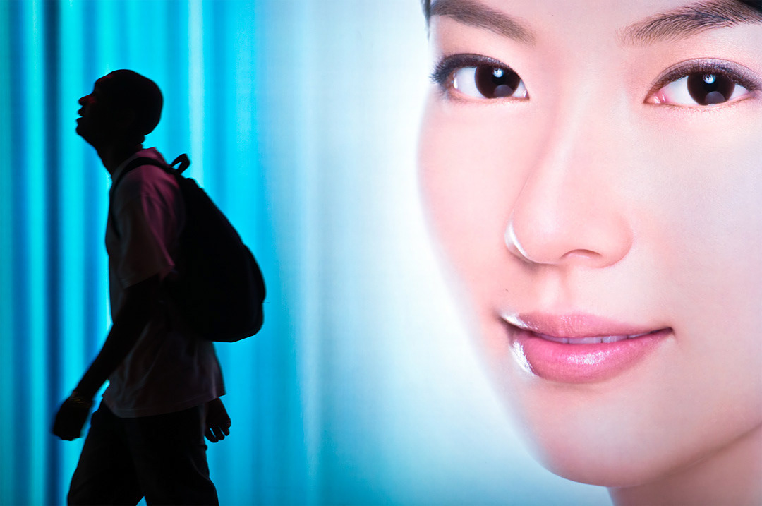 A man walking in front of a advertisement in Hong Kong. 