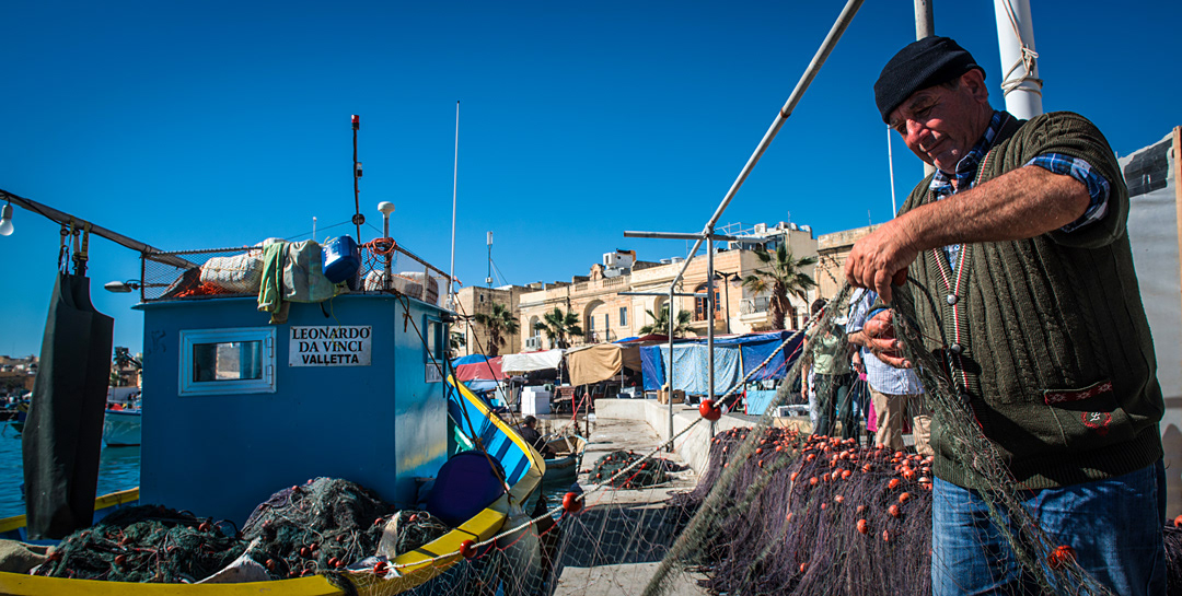 Fisherman working along his boat at Marsaxlokk's harbour. 