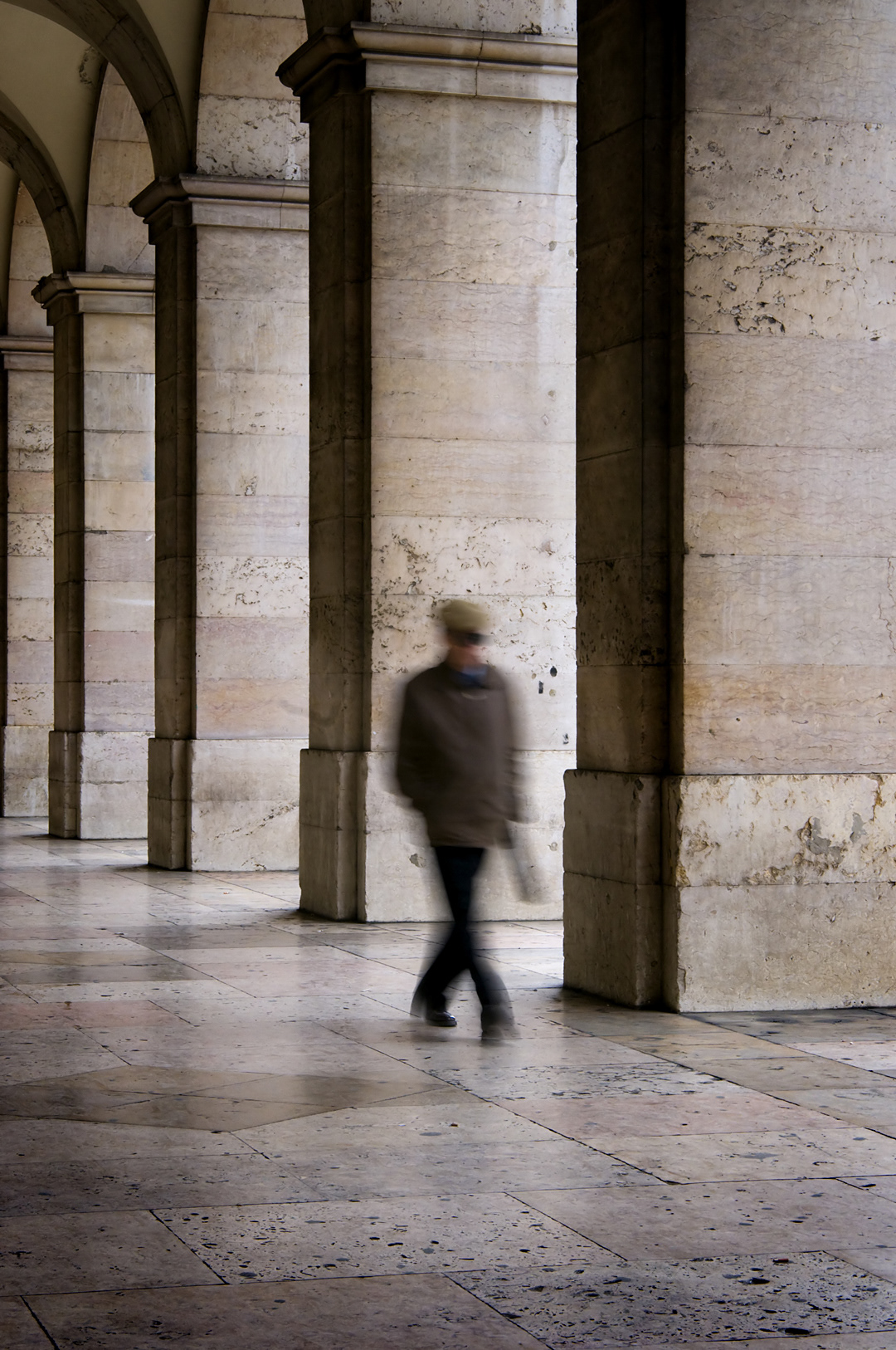 A man walking under the Plaça do Comercio arcades. 