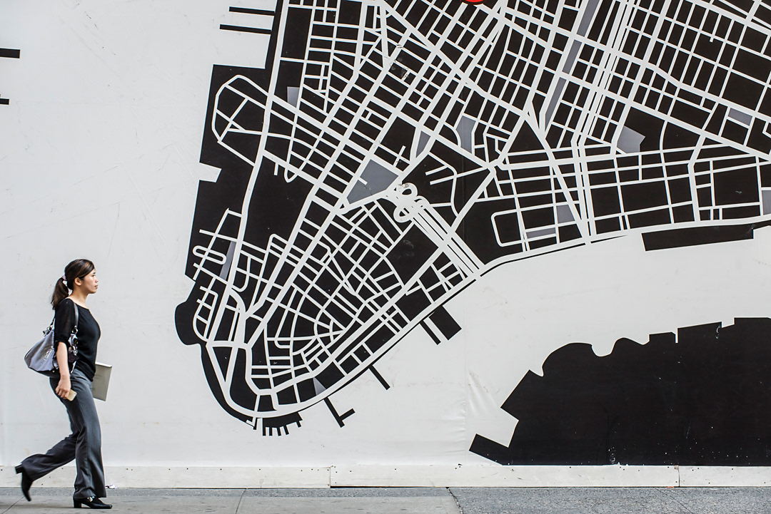 A woman crossing in front of a map of Manhattan. 