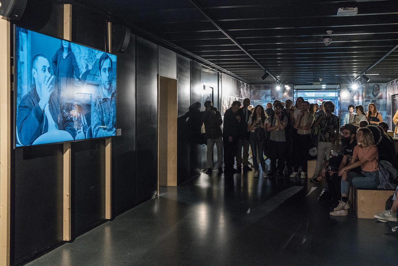 A group of people gathered at the exhibition watching a screening of Joaquim Jorda's movie.
