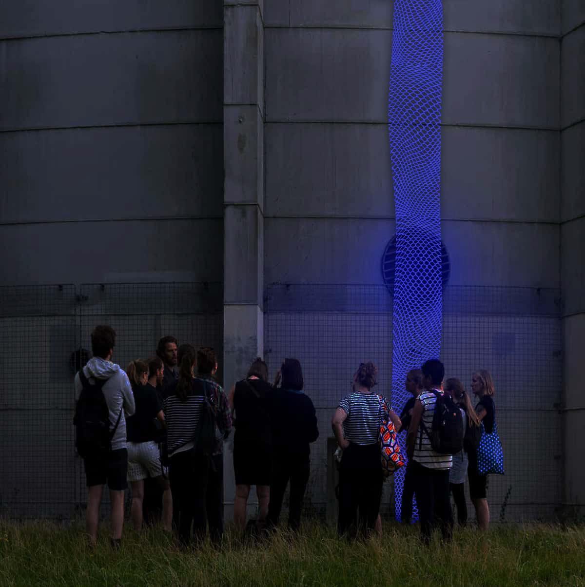 Close up view of a group of people standing at the bottom of the tower, looking at the blue mesh light of the installation.