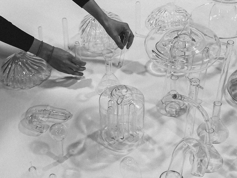 Several glass pieces scattered across the table, with partial view of a person repositioning them.