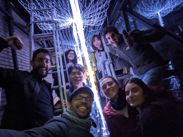 Students standing on ladders underneath the tied fiber optic light installation.