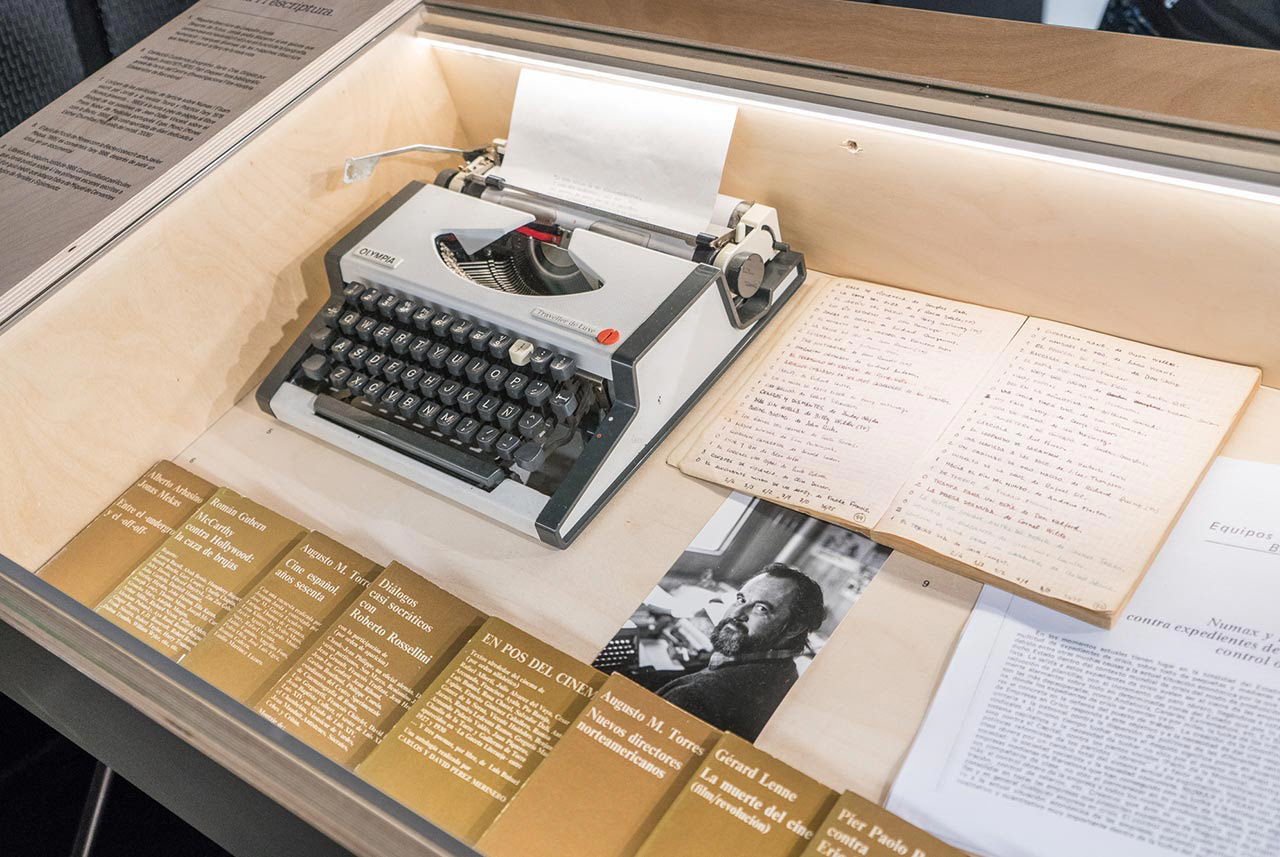 A typewriter, notebook, photograph, and a script on display in a wooden case.