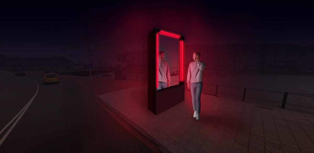 A person standing in front of the red light sculpture looking at their reflection.