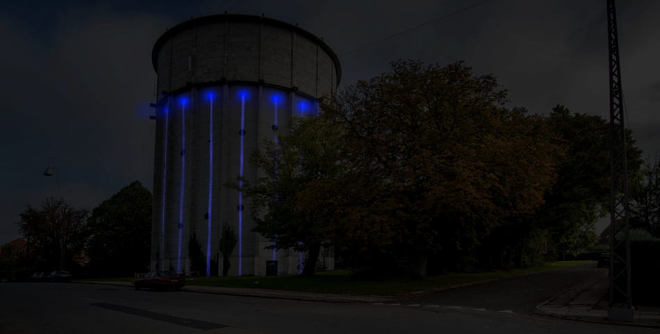 Full view of the water tower from the street, showing the full light installation and all lighting elements.