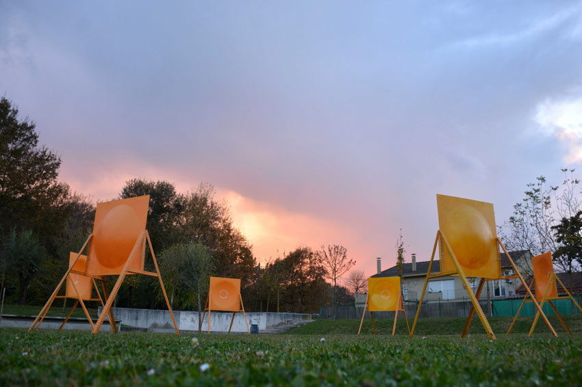 6 orange sound mirrors scattered across a field in a circular form pointed towards the center