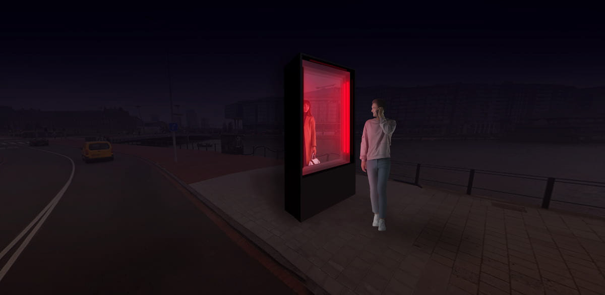 A person standing in front of the red light sculpture seeing someone on the other side of the glass..