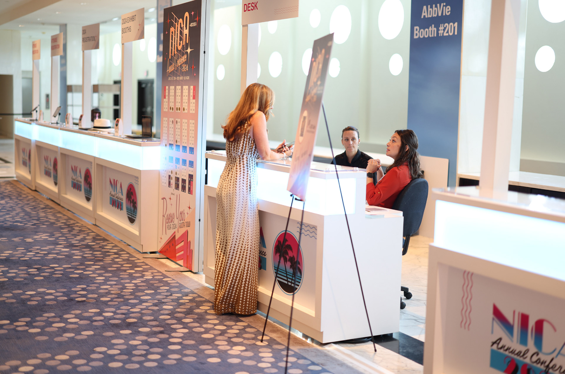 NICA 2023 registration area with branded counter panels, palm graphics, and overhead check-in signs at Fontainebleau Miami Beach.