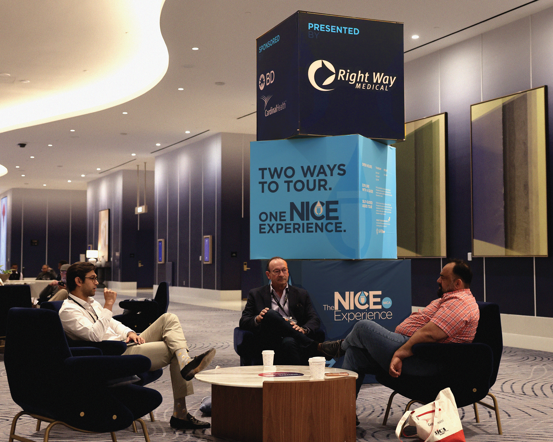 Attendees seated beside The NICE Experience cube stack, displaying branded tour information and sponsor logos at the NICA Annual Conference.