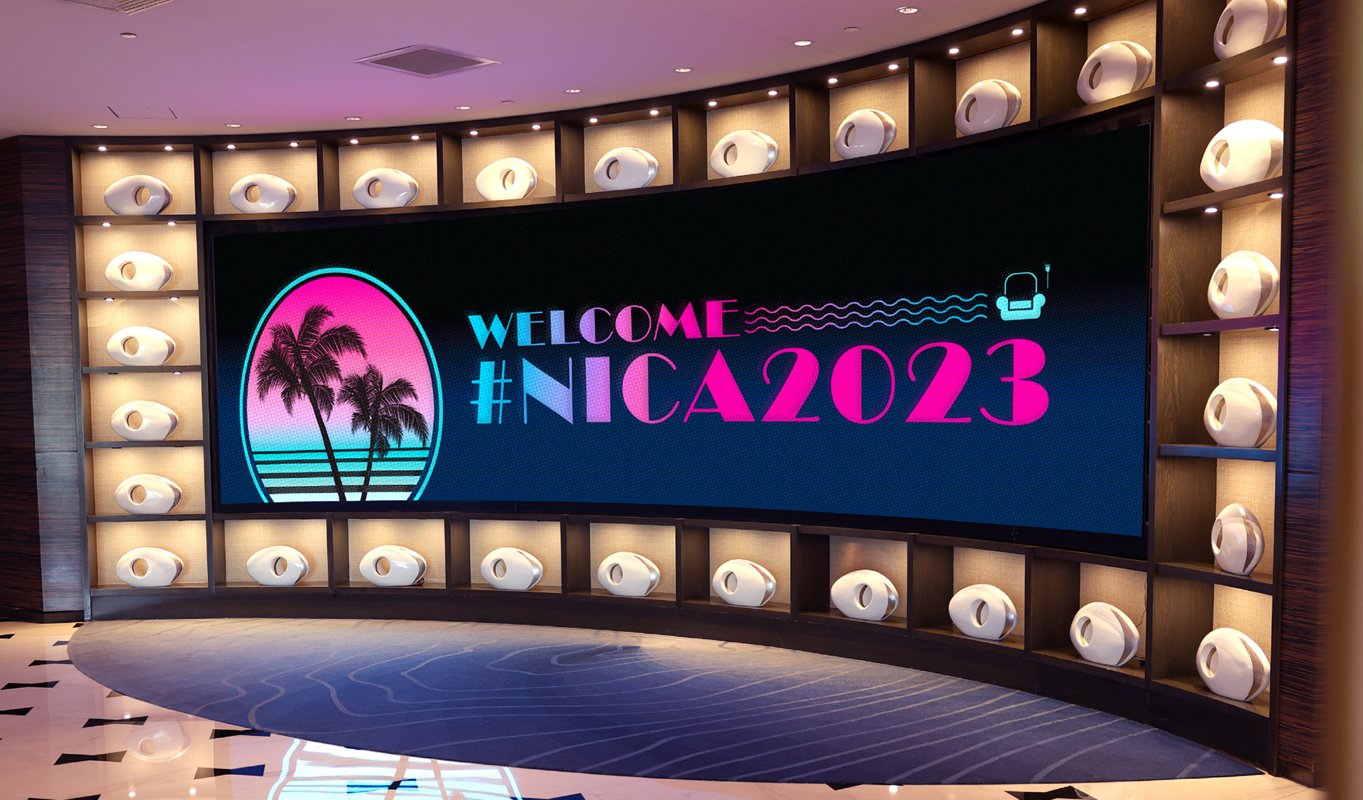 Curved LED lobby display at Fontainebleau Miami Beach showing NICA 2023 welcome graphics with palm silhouettes and aqua and magenta branding.