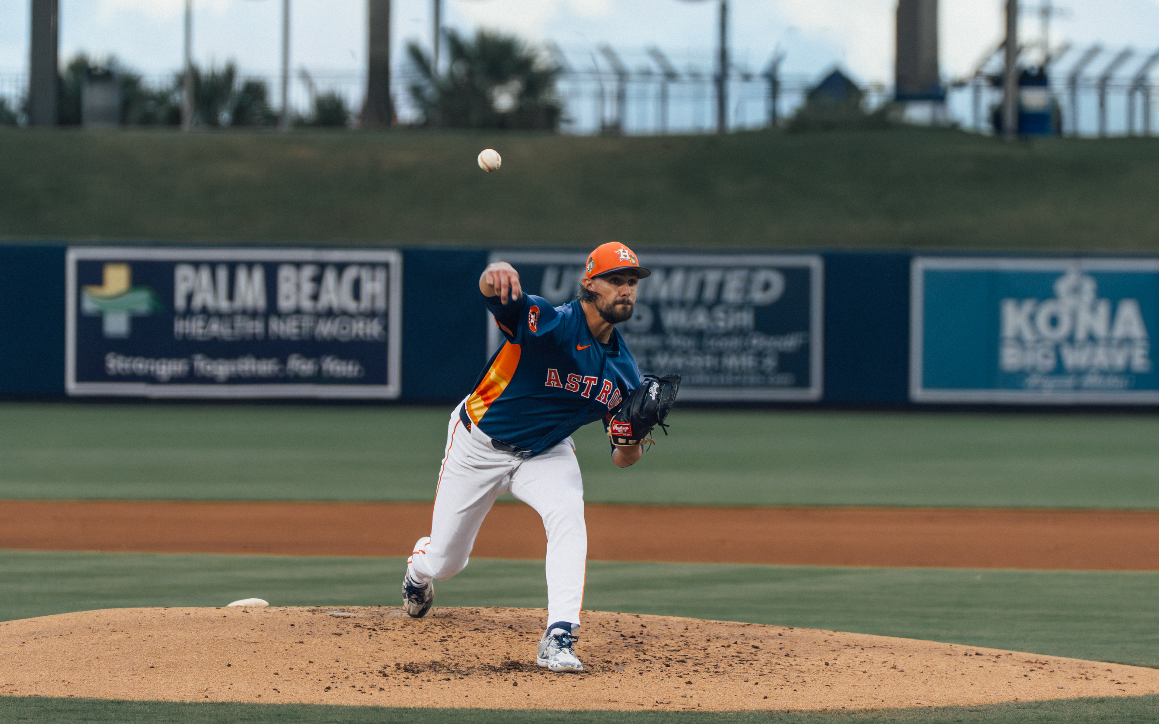 Astros pitcher releasing the ball, daylight shot which means this was likely early in the game during warmups or the first inning. Palm Beach Health Network signage visible in the background. The ball is frozen right at the release point which is a nice capture.  From the box score, the Astros pitchers in order were Logan VanWey, Peter Lambert, Ryan Weiss, and Roddery Muñoz. Since this looks like a daytime/early evening shot and the game started at 6:05 PM, this could be from early innings. Can you see the jersey number?  Based on build and delivery, this could be Peter Lambert who pitched 3 innings, or Ryan Weiss who got the win pitching 4.1 innings.  Alt text: Houston Astros pitcher delivers from the mound with the ball at the release point during a spring training game against the New York Mets at The Ballpark of the Palm Beaches, March 2026. Photo by Aday's Media Production