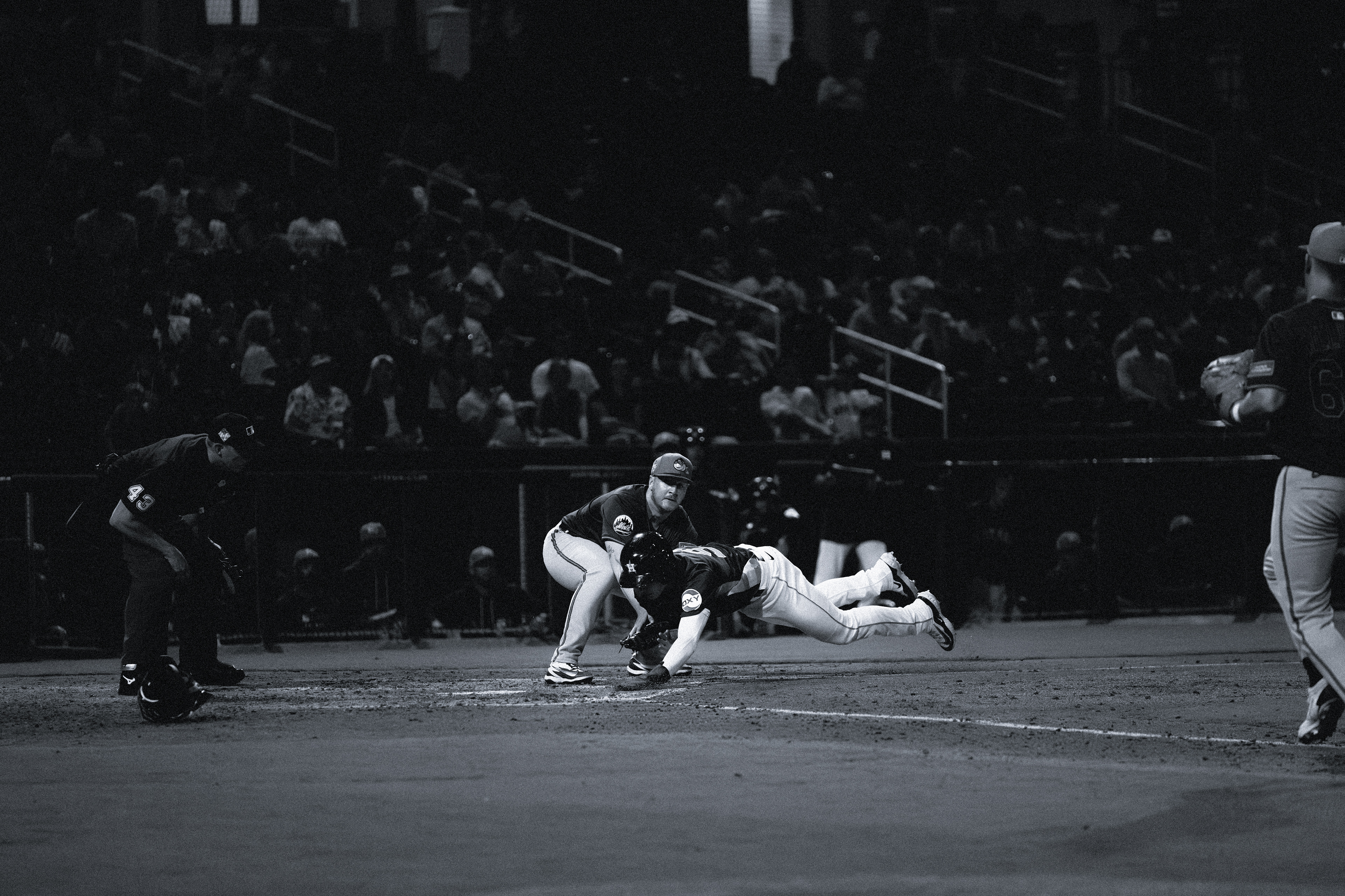 Houston Astros runner dives headfirst into home plate as the umpire watches the play during a spring training game against the New York Mets at The Ballpark of the Palm Beaches, March 2026. Black and white edit. Photo by Aday's Media Production