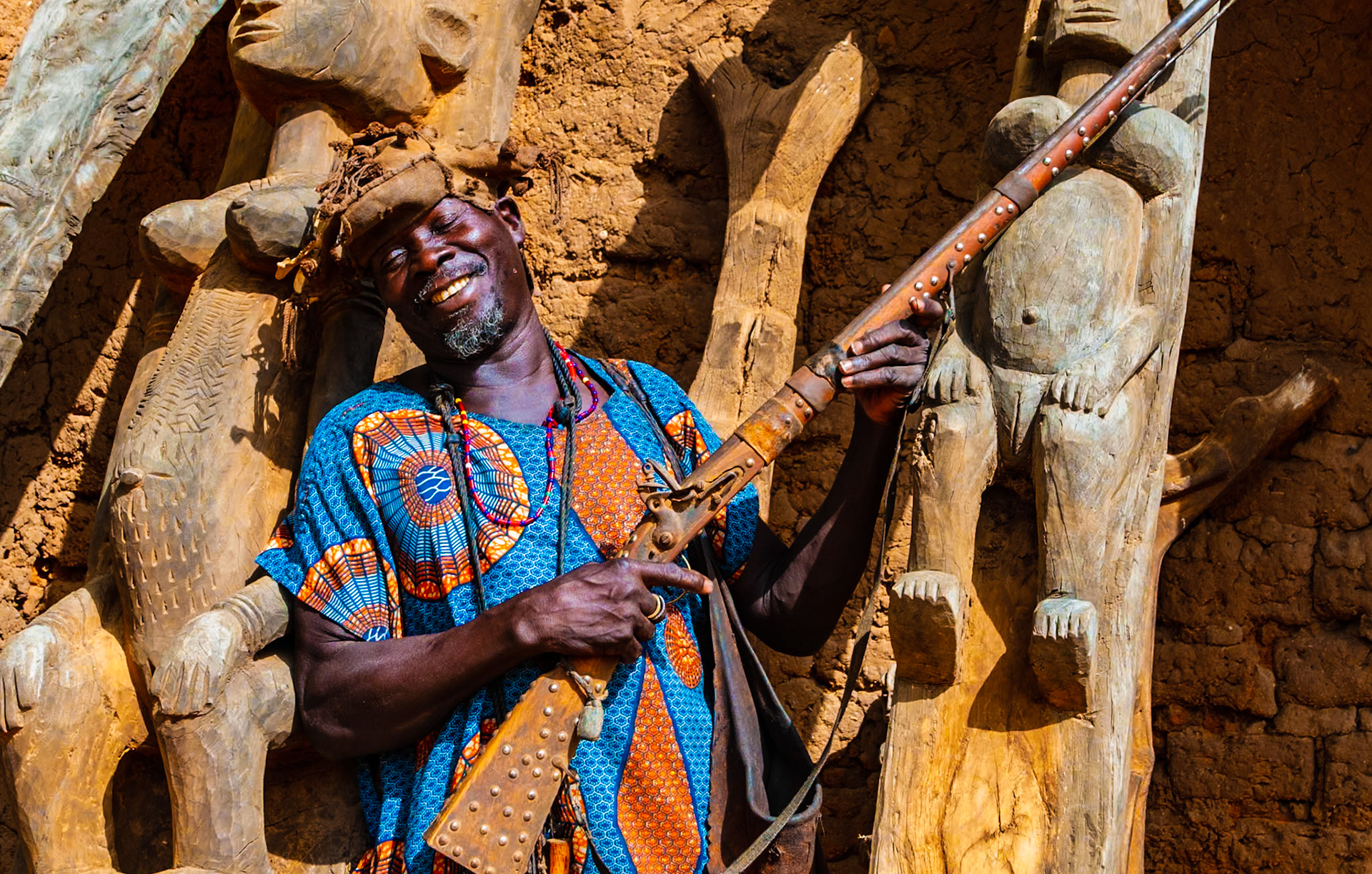 A Dogon hunter in Mali proudly shows off his flintlock rifle and carving handiwork. In this remote community, the hunter serves as a link between the village and the bush. However, desertification and years of overhunting have severely depleted the local wildlife. Once found in abundance, the large herbivores are gone. Now, only smaller mammals such as monkeys are prey for the hunter's rifle.